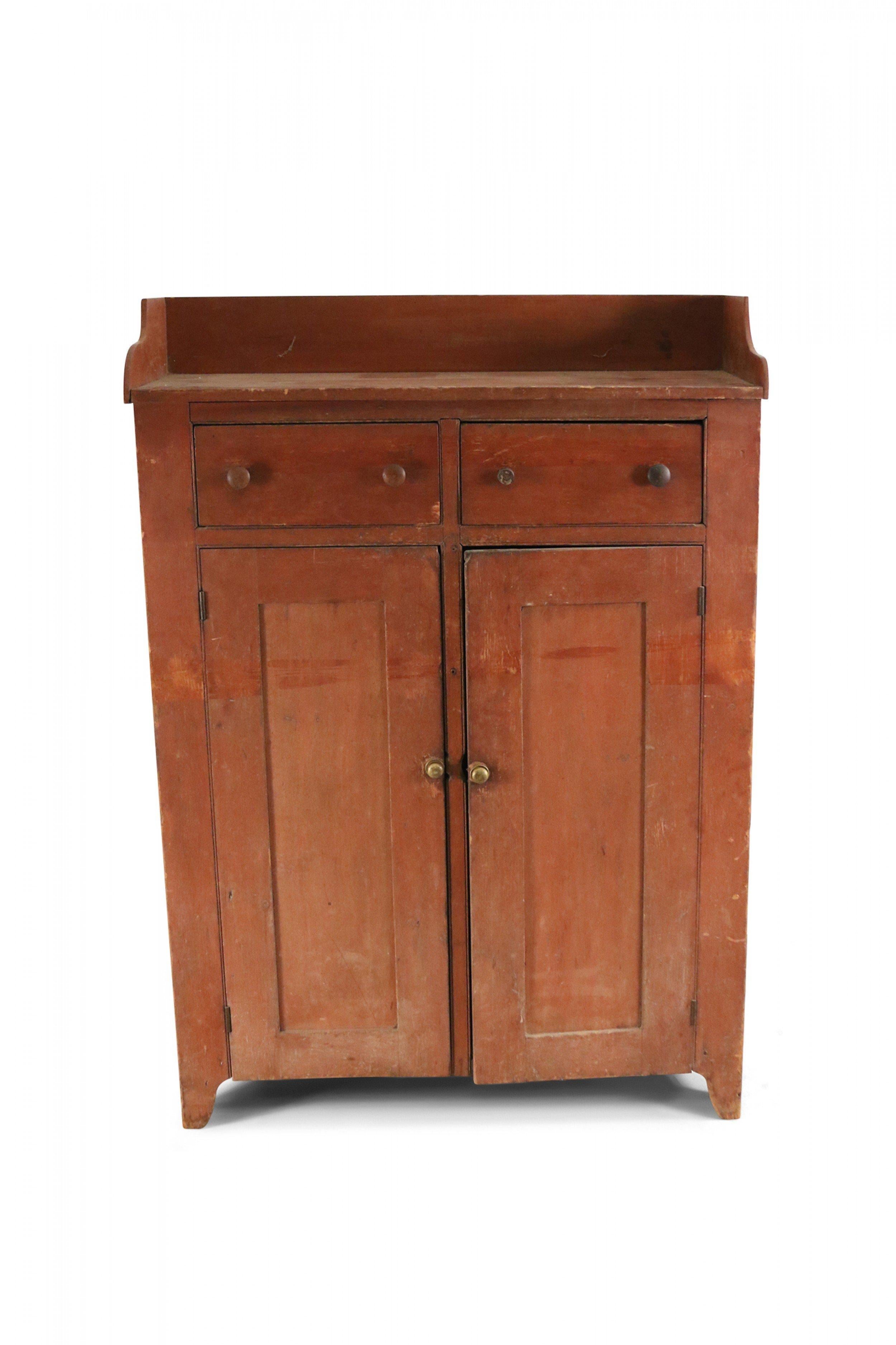 American Country-style (19/20th Century) stained pine wood storage cabinet with two hinged cabinet doors under two drawers with wooden drawer and cabinet pulls and a partial gallery around the top.
 