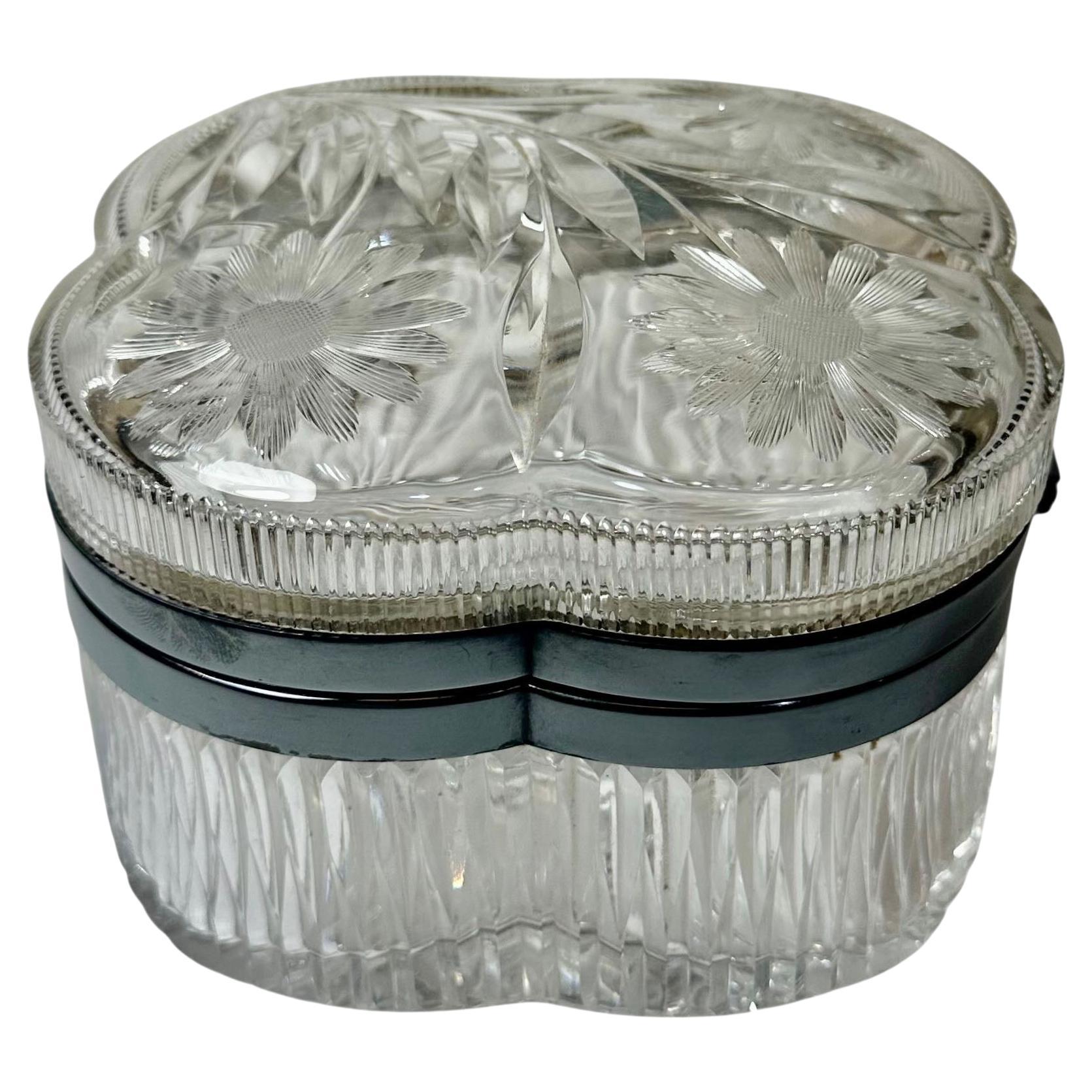 An elegant 1940s American cut crystal box featuring a silver plate edge and a beautifully detailed design. The lid is adorned with three finely cut daisies, adding a delicate floral touch to the crisp geometry of the crystal.

This piece is in