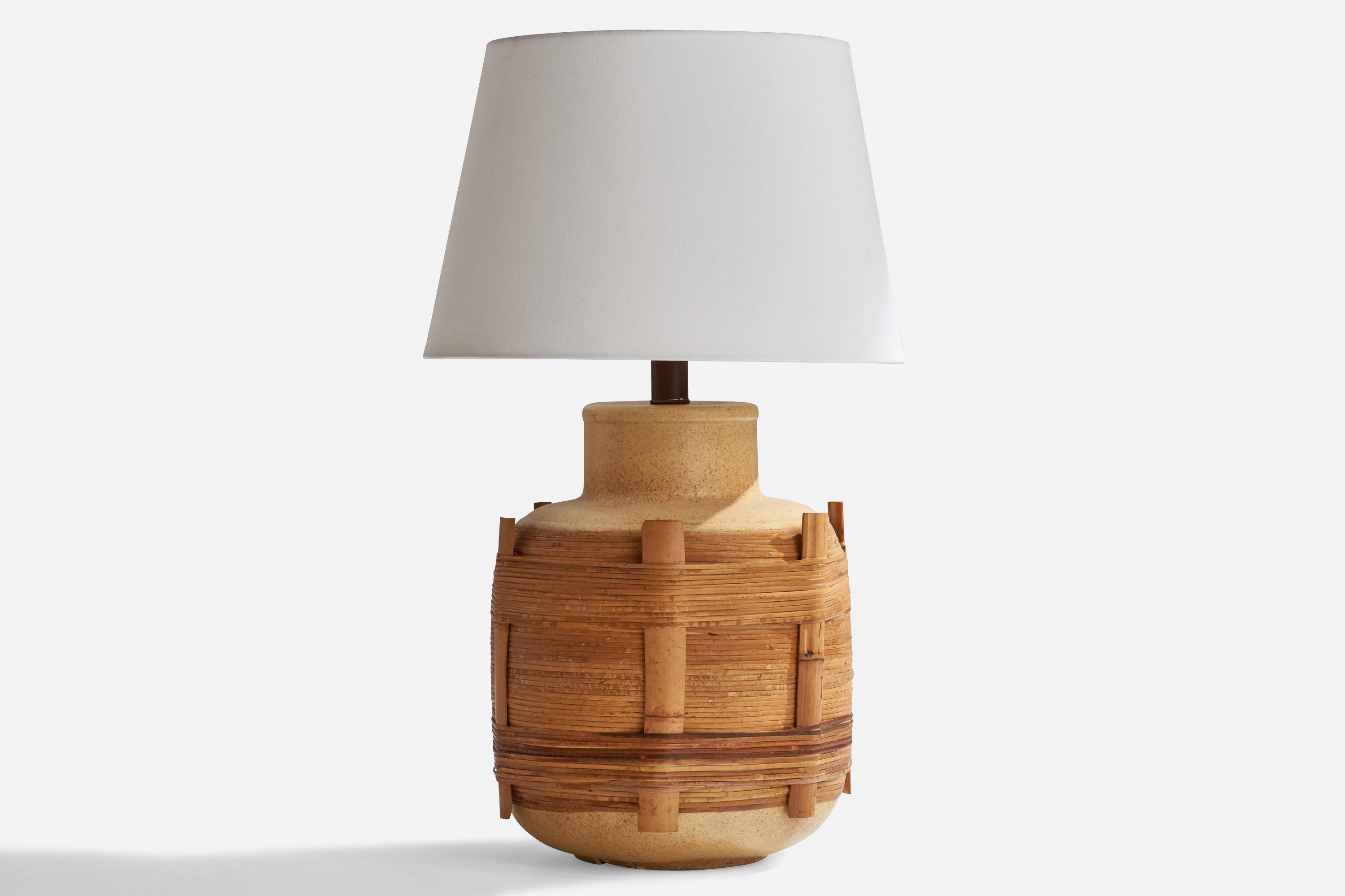 A beige-glazed ceramic, bamboo and rattan table lamp designed and produced in the US, c. 1950s.

Dimensions of Lamp (inches): 21.5”  H x 12” Diameter
Dimensions of Shade (inches): 12”Top Diameter x 16”  Bottom Diameter x 11.75” H
Dimensions of Lamp