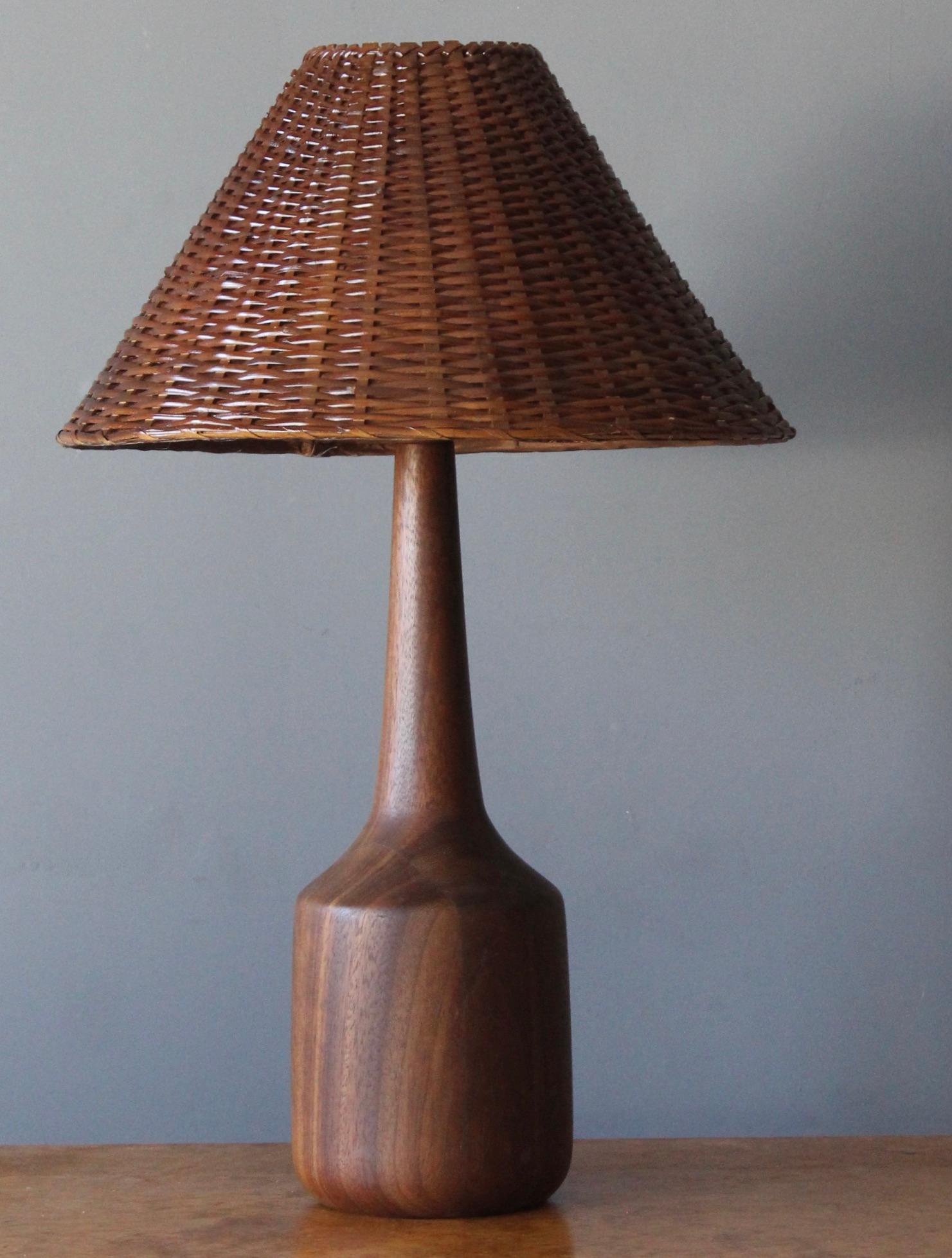 A table lamp, designed and produced in United States, 1960s. Features finely turned solid teak. brass, assorted vintage rattan lampshade. With beautiful original patina.

Stated dimensions include lampshade. Illustrated vintage rattan lampshade