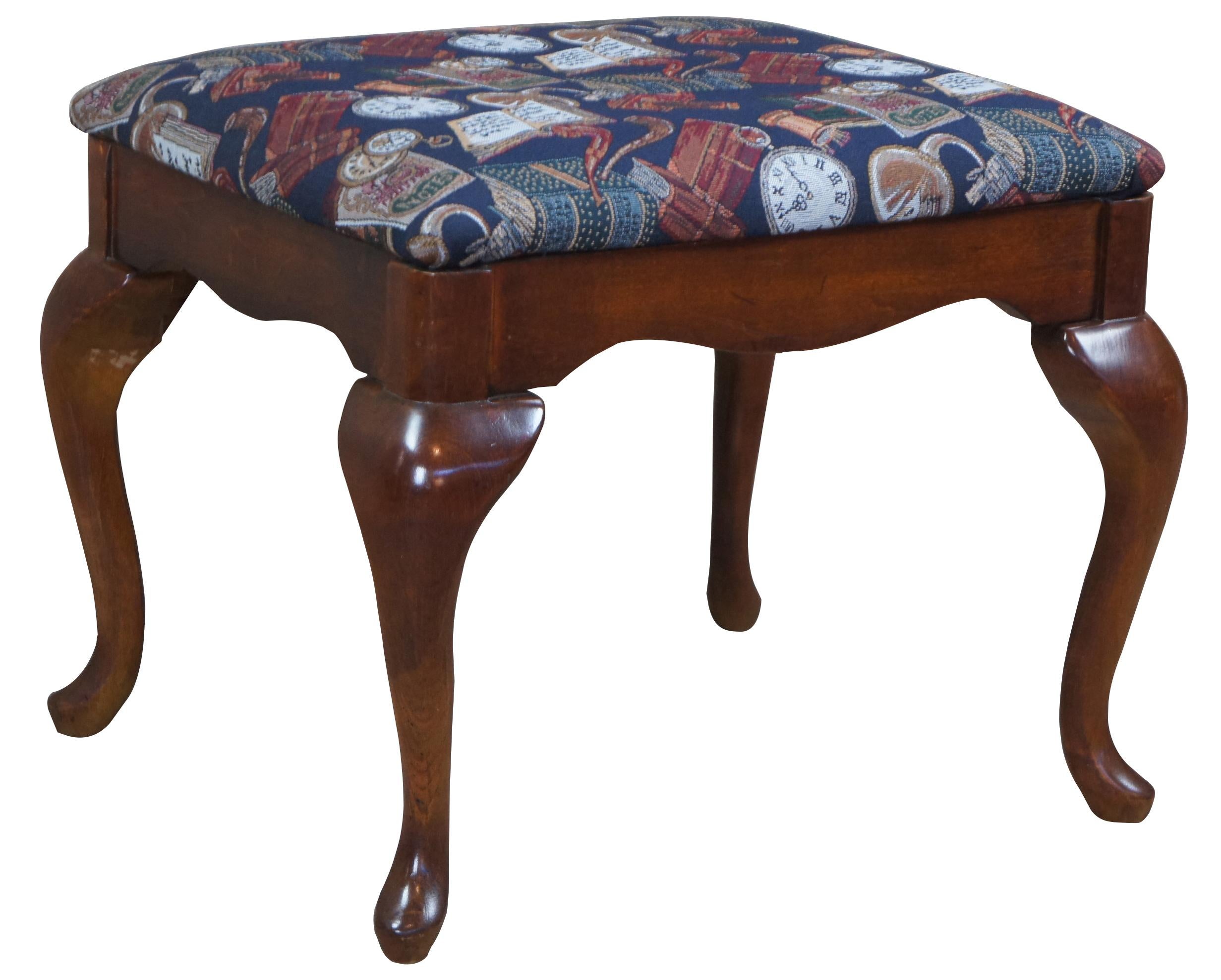 American drew stool, circa 1980s. Made from cherry in Queen Anne styling with cabriole legs leading to pad feet. Includes a serpentine cut apron and blue upholstery library theme with clocks, books, pipes and music.
  