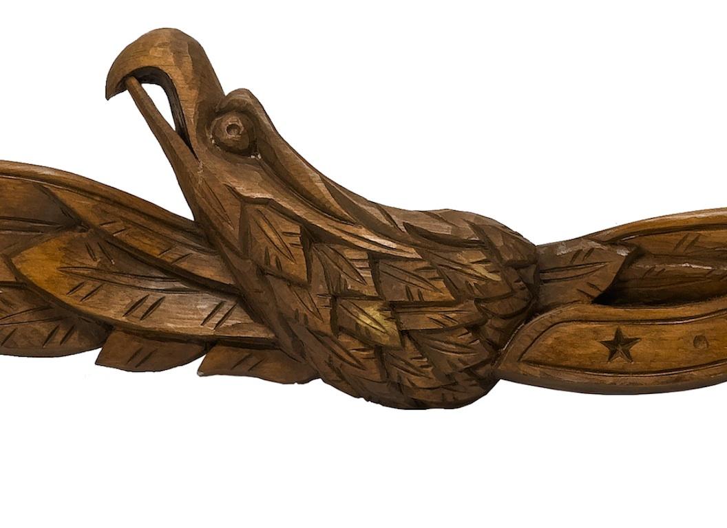 This is a hand-carved American folk eagle. This particular example is quite unique and depicts a spread wing eagle, head turned to right, with a distinctive beak. Wrapped around the eagle is a carved ribbon with the two stars and inscribed Latin