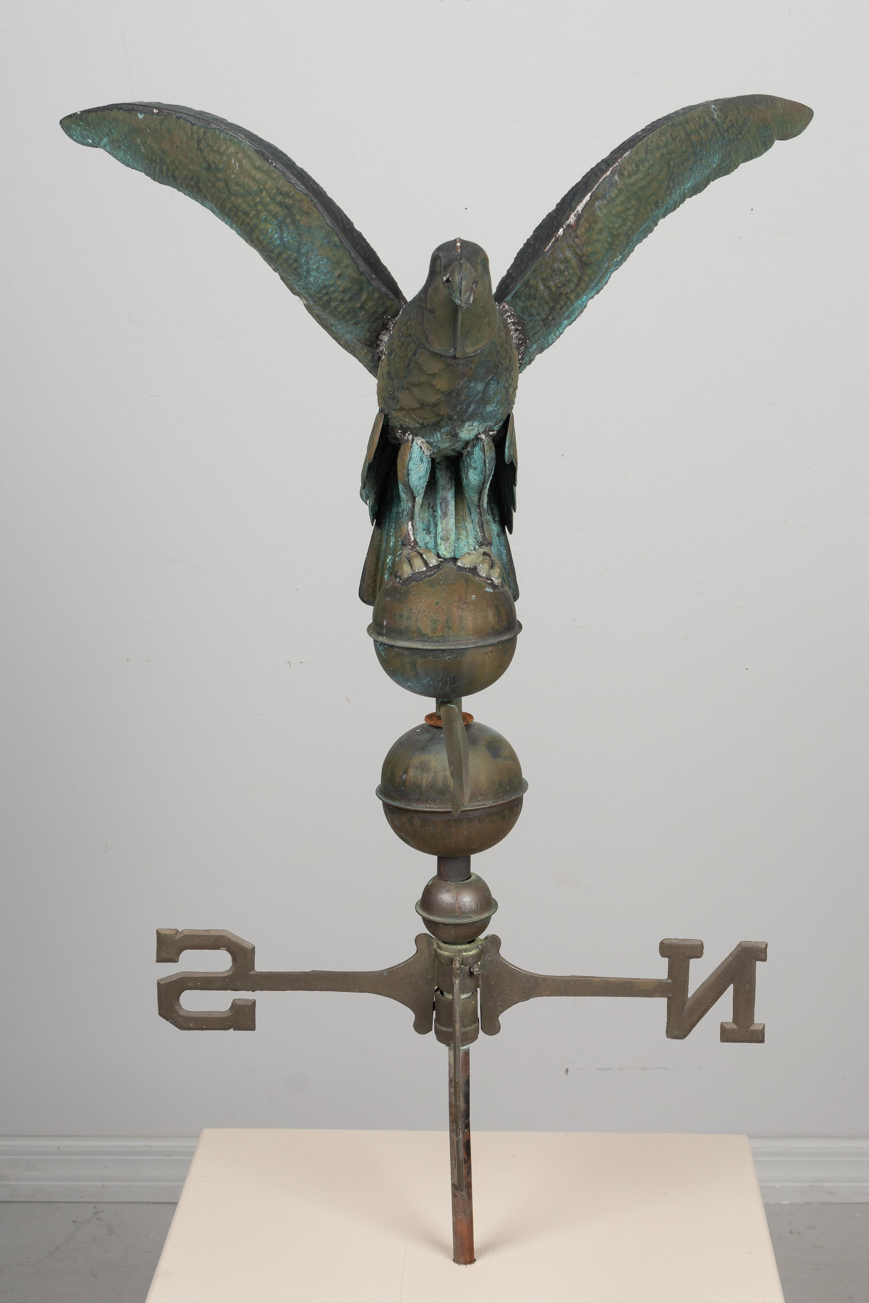 A vintage American weathervane with an eagle perched an a globe, wings outstretched. The eagle and globes are made of welded copper and have a nice weathered verdigris patina. The directionals are solid brass and are 18