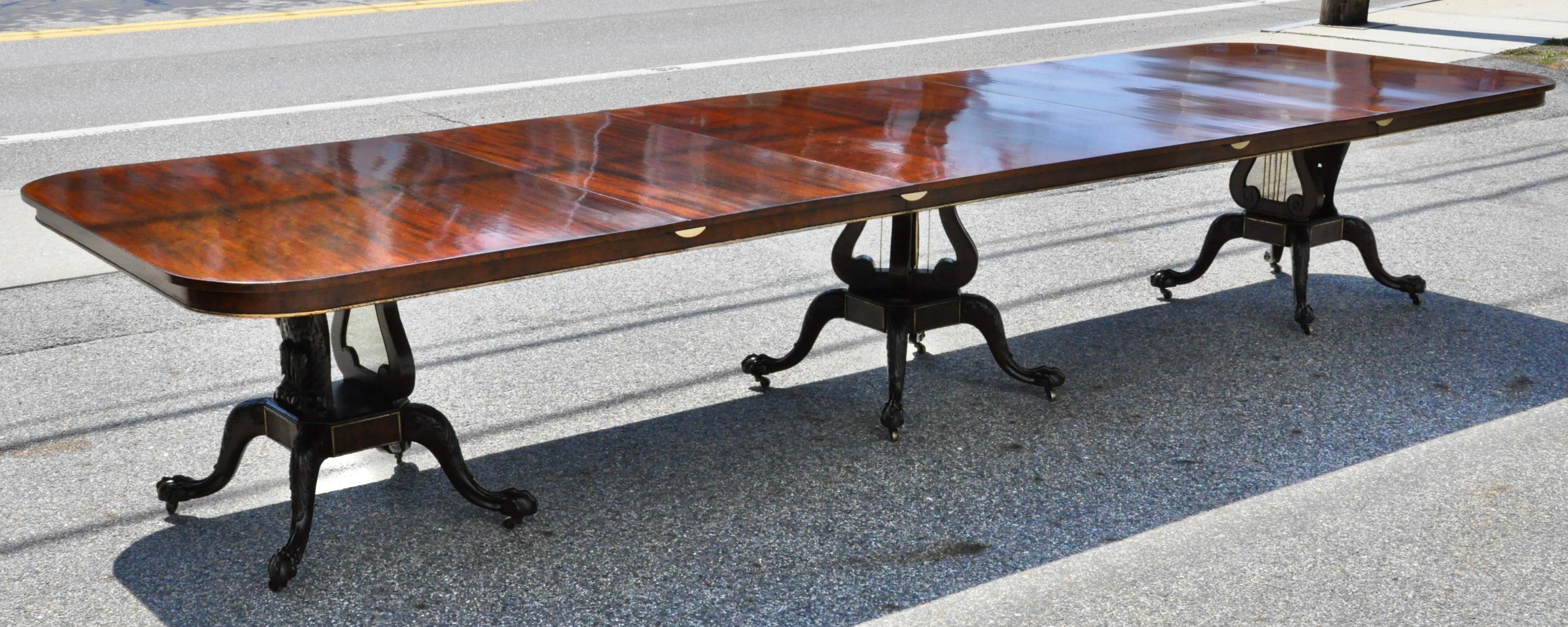 American solid mahogany three pedestal dining table with two original additional leaves

In the style of Duncan Phyfe with carved patriotic American Eagles on end pedestals and brass stringed lyres on middle pedestal. Brass banding throughout.