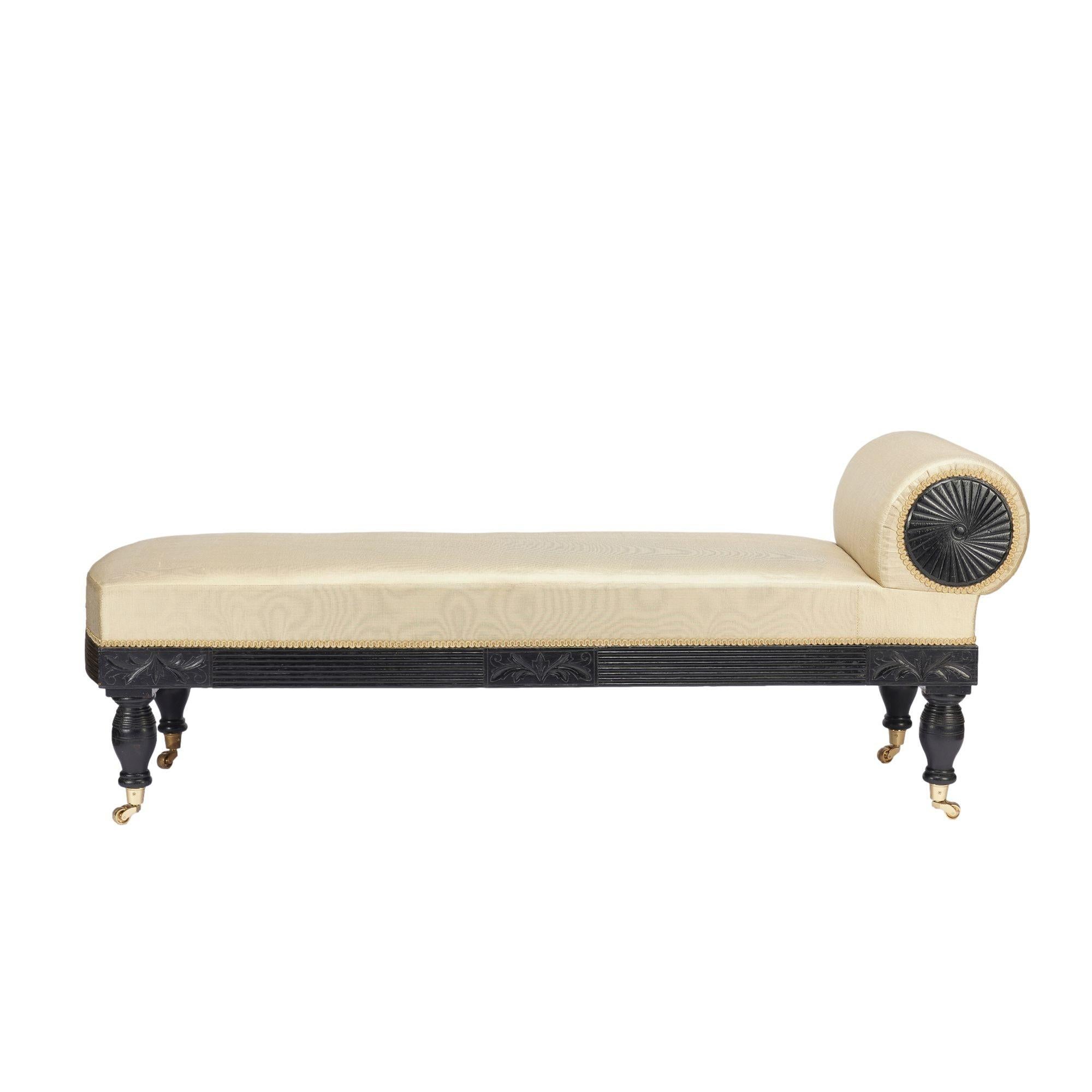 Signed American Eastlake upholstered chaise with an ebonized and reeded maple frame resting on four turned legs fitted with cast brass cup casters. Both sides of the bolster are fitted with round, ebonized panels that match the frame, and feature a