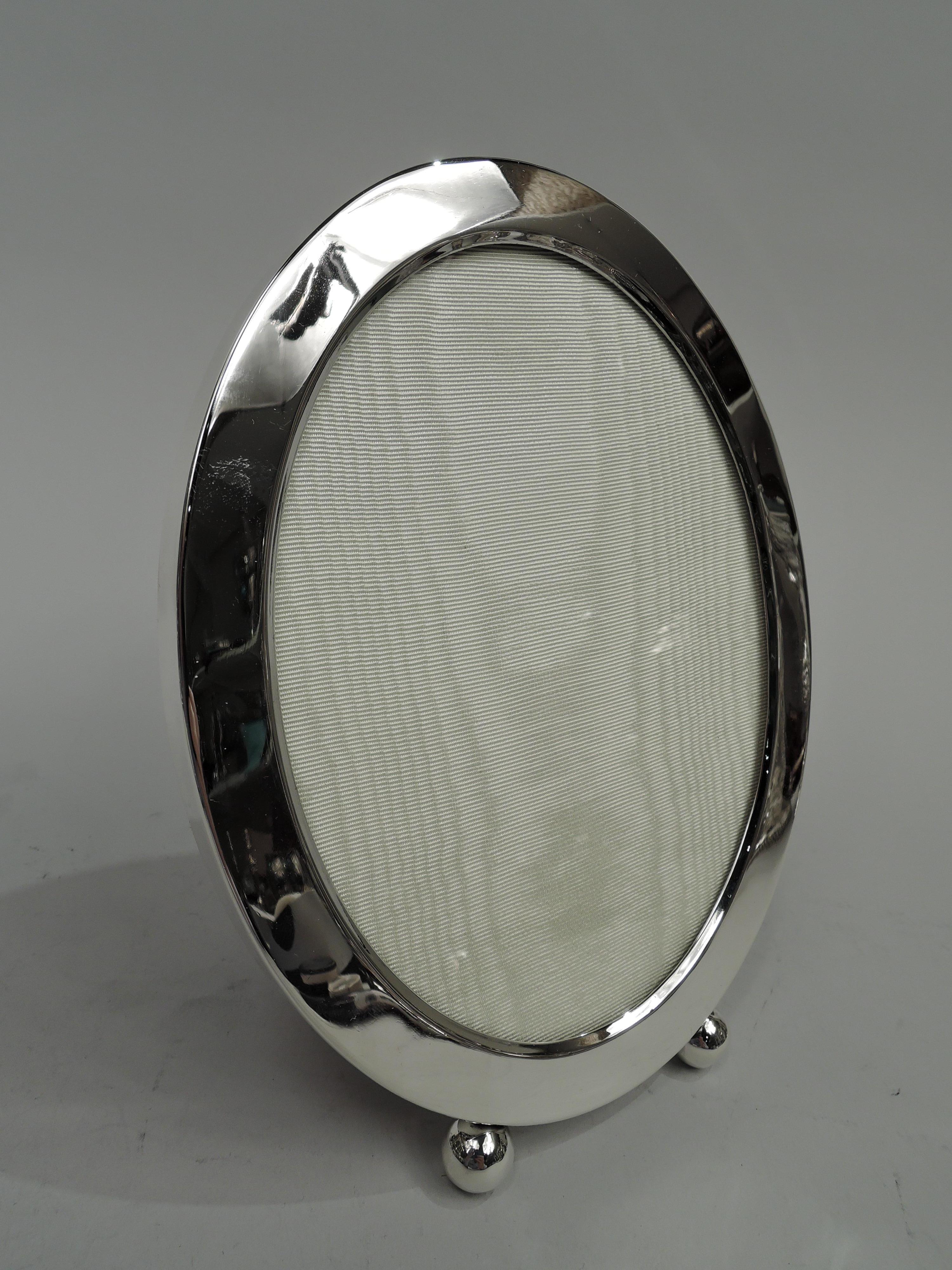 American Edwardian Modern sterling silver picture frame, ca 1910. Oval window in same surround with canted interior border and flat sides. Two ball supports. Simple and unadorned for the perfect portrait. With glass, silk lining, and red velvet back