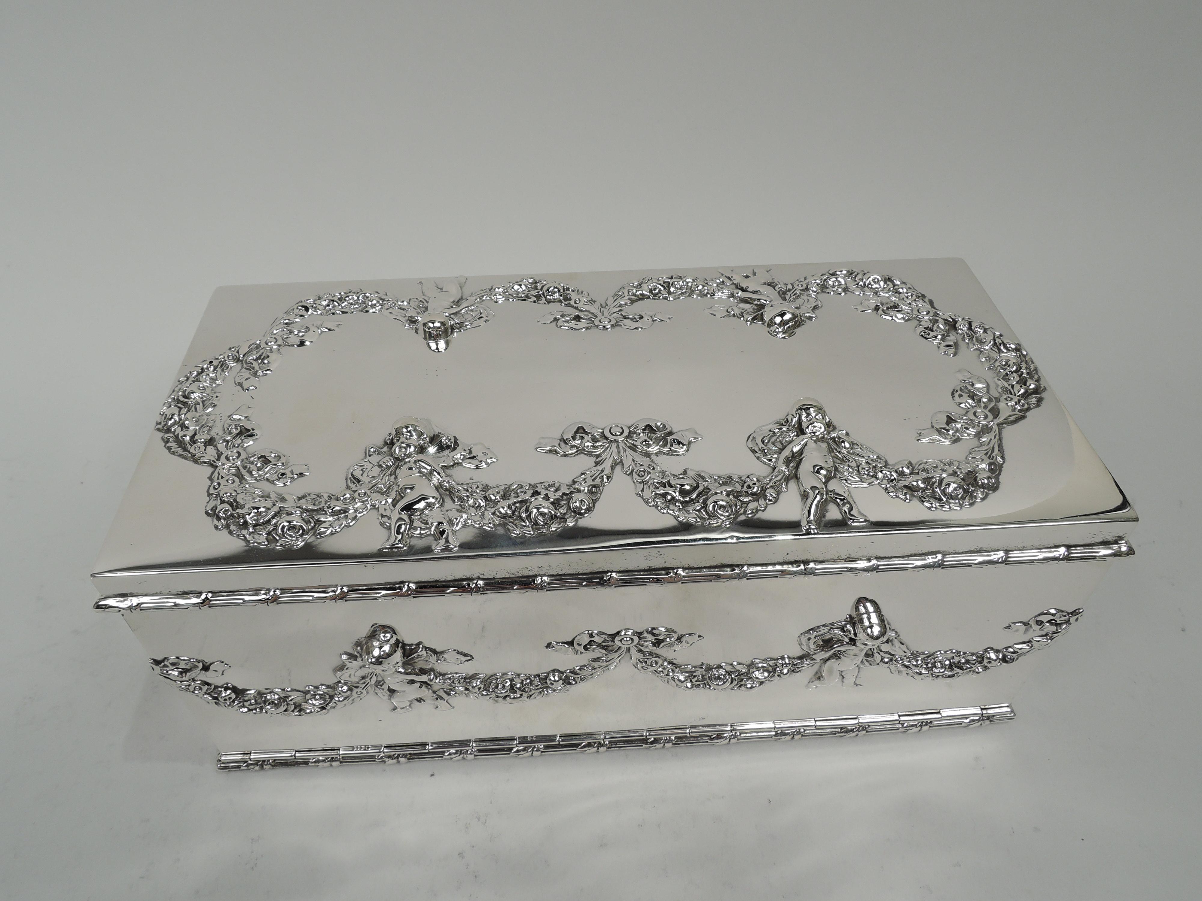 Edwardian Regency sterling silver jewelry box. Made by William B. Durgin in Concord, ca 1910. Rectangular with straight sides and hinged drop-front. Cover hinged and flat. On sides, wraparound garland held-up by sweet bare-bottomed cherubs. Cover