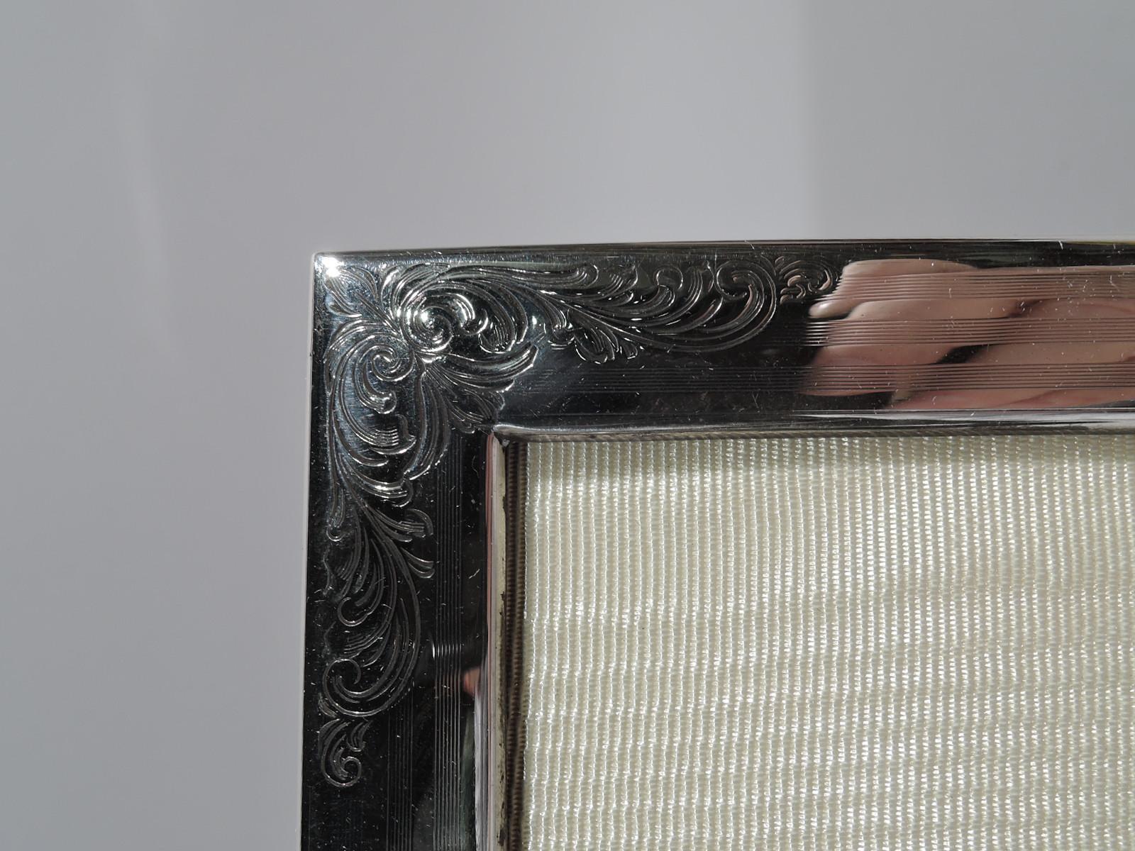 Edwardian sterling silver picture frame. Made by William B. Kerr in Newark, circa 1910. Rectangular window in surround with engine-turned wraparound pinstripes and engraved leafing scrolls at corners. Tubular cartouche (vacant). With glass, silk