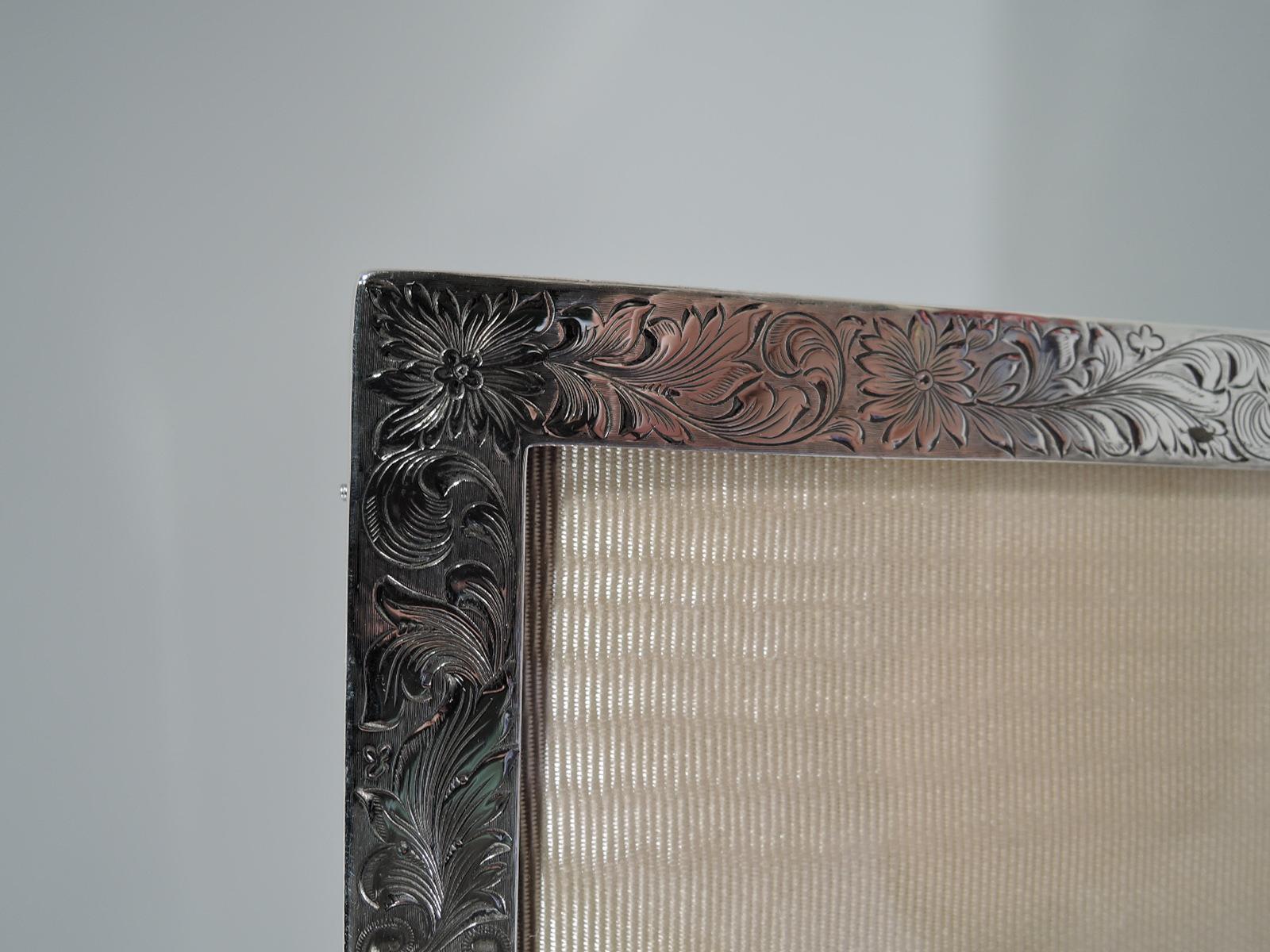 Edwardian sterling silver picture frame. Made by Meriden Britannia (a division of International) in Meriden, Conn. Rectangular window and flat surround engraved with fluid foliage and flowers. Two shaped cartouches (vacant). With glass, silk lining,