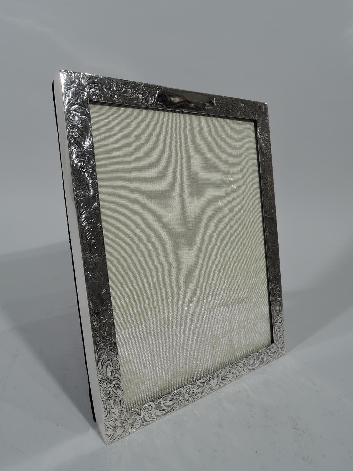 Edwardian sterling silver picture frame. Rectangular window and flat surround engraved with dense flowers and foliate scrolls. Shaped cartouche (vacant). For vertical (portrait) display. With glass, silk lining, and velvet back and hinged support.