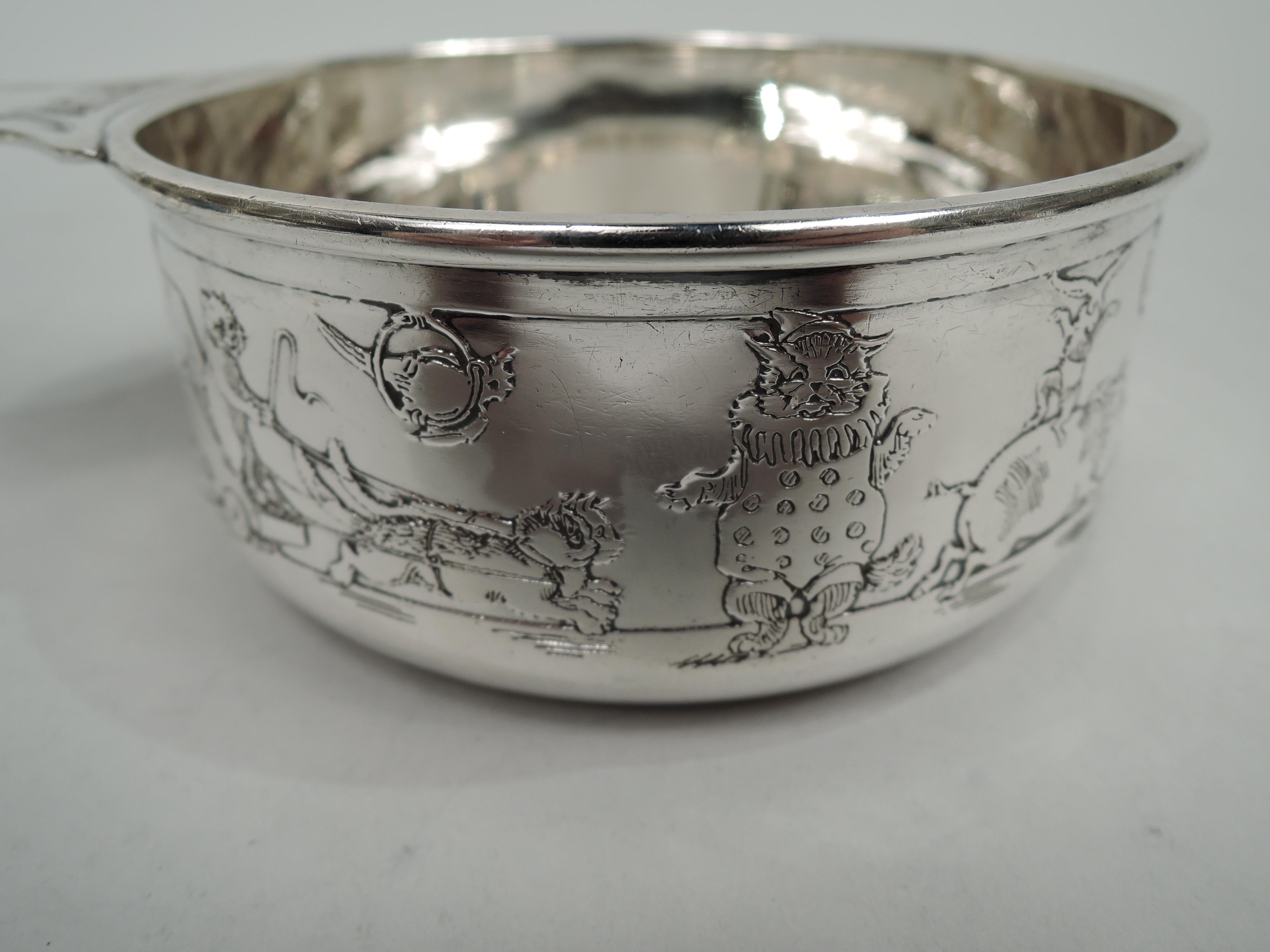 Edwardian sterling silver porringer with circus motif. Made by William B. Kerr in Newark, ca 1910. Upward tapering sides and molded rim. Solid and waisted handle. Acid-etched procession with piggies, kitties, and doggies as well as elephants and