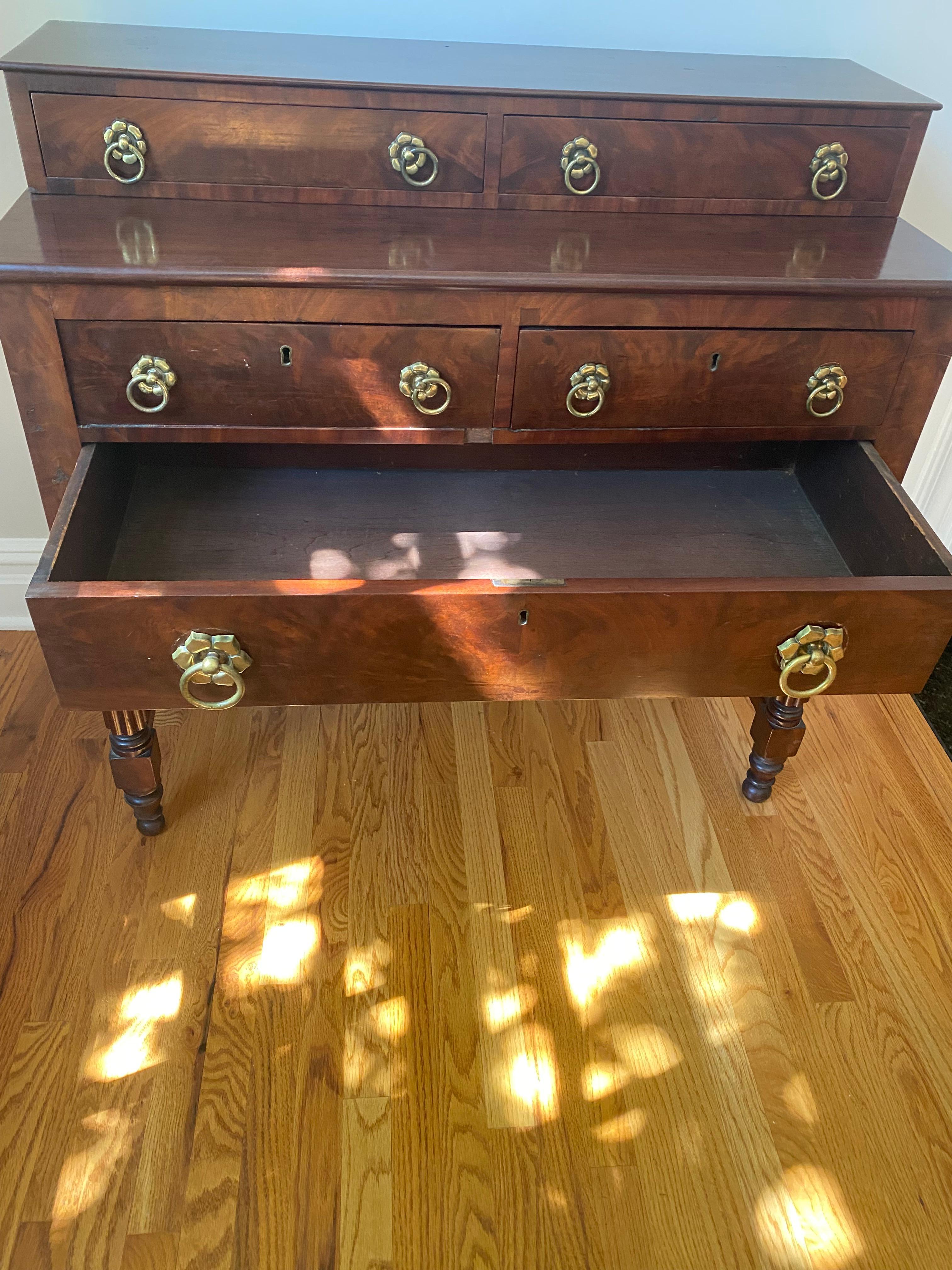 Lovely antique 19th century mahogany American Empire sideboard having two levels. Top level has two drawers; bottom section has two smaller drawers over one large drawer. Beautiful original brasses and pretty turned legs with stretcher.