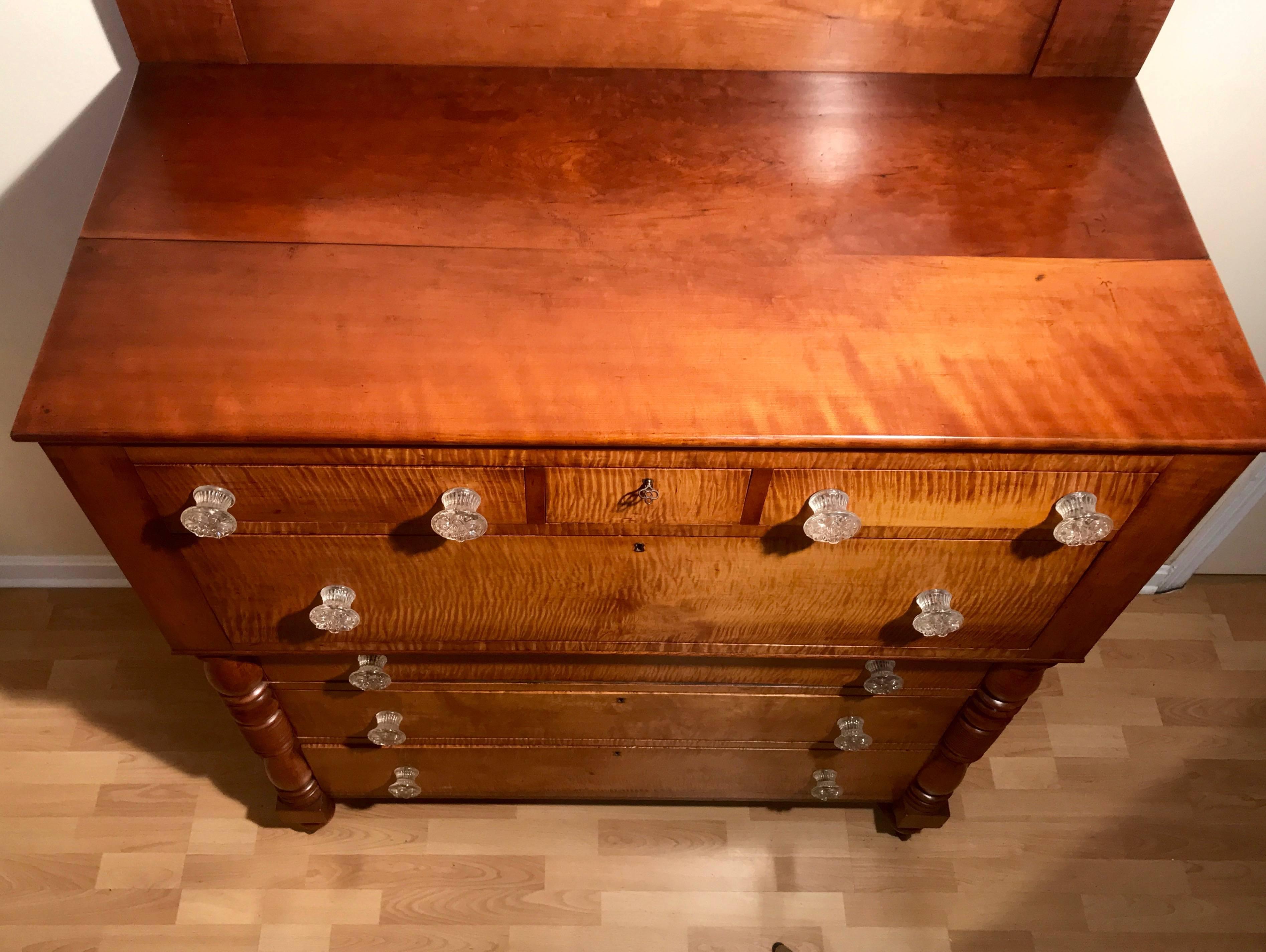 American Empire chest of drawers circa 1840 in tiger maple and cherry. Turned columns and feet, backsplash in cherry with Tiger maple veneered chimneys. Hand dovetailed drawers. All original glass hardware in excellent condition. Unusual top center