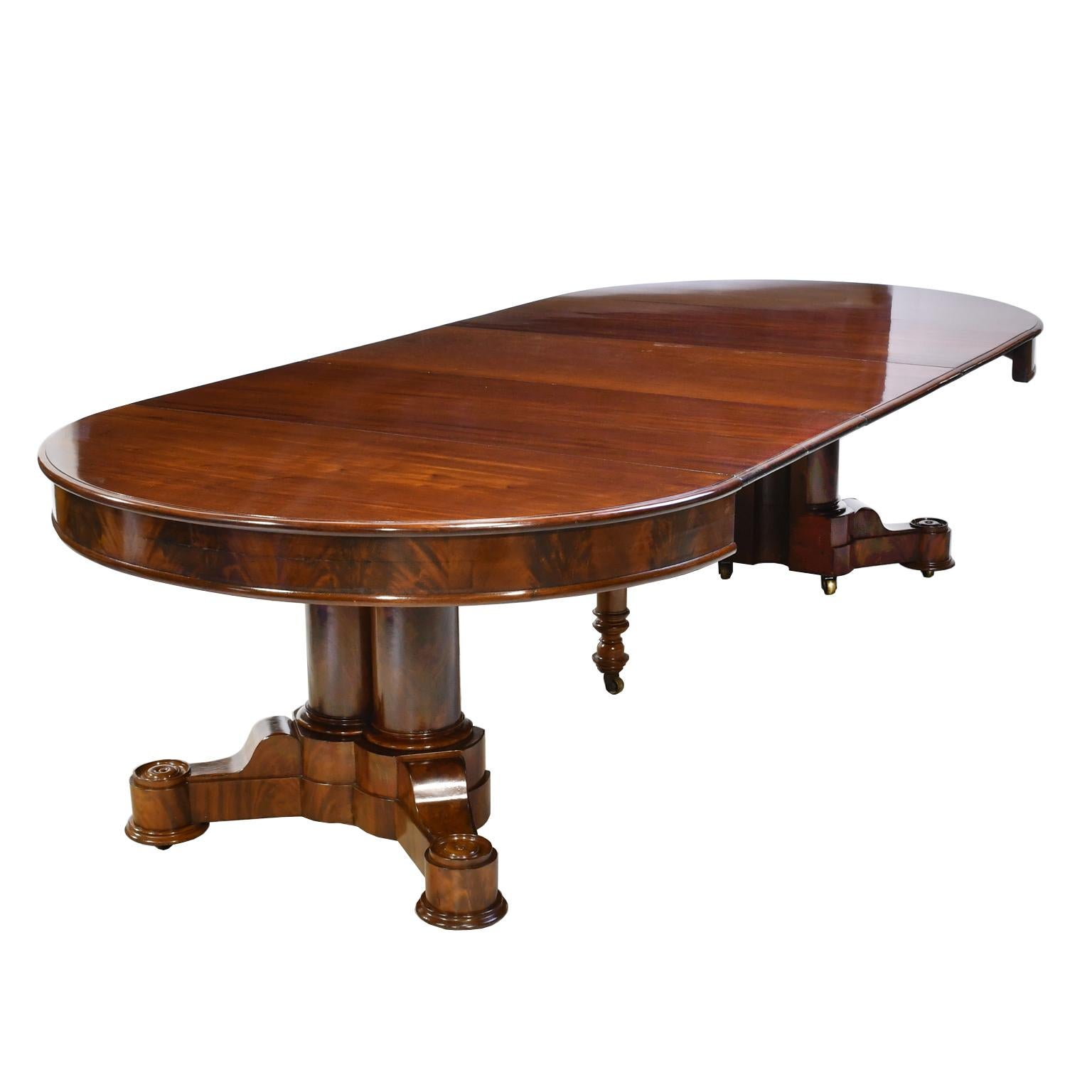 A very beautiful and functional American Empire dining table in mahogany in the manner of renown cabinetmaker, Anthony Gabriel Quervelle (1789-1856), Philadelphia, circa 1840. Features racetrack / oval top over a cluster pedestal with four turned,