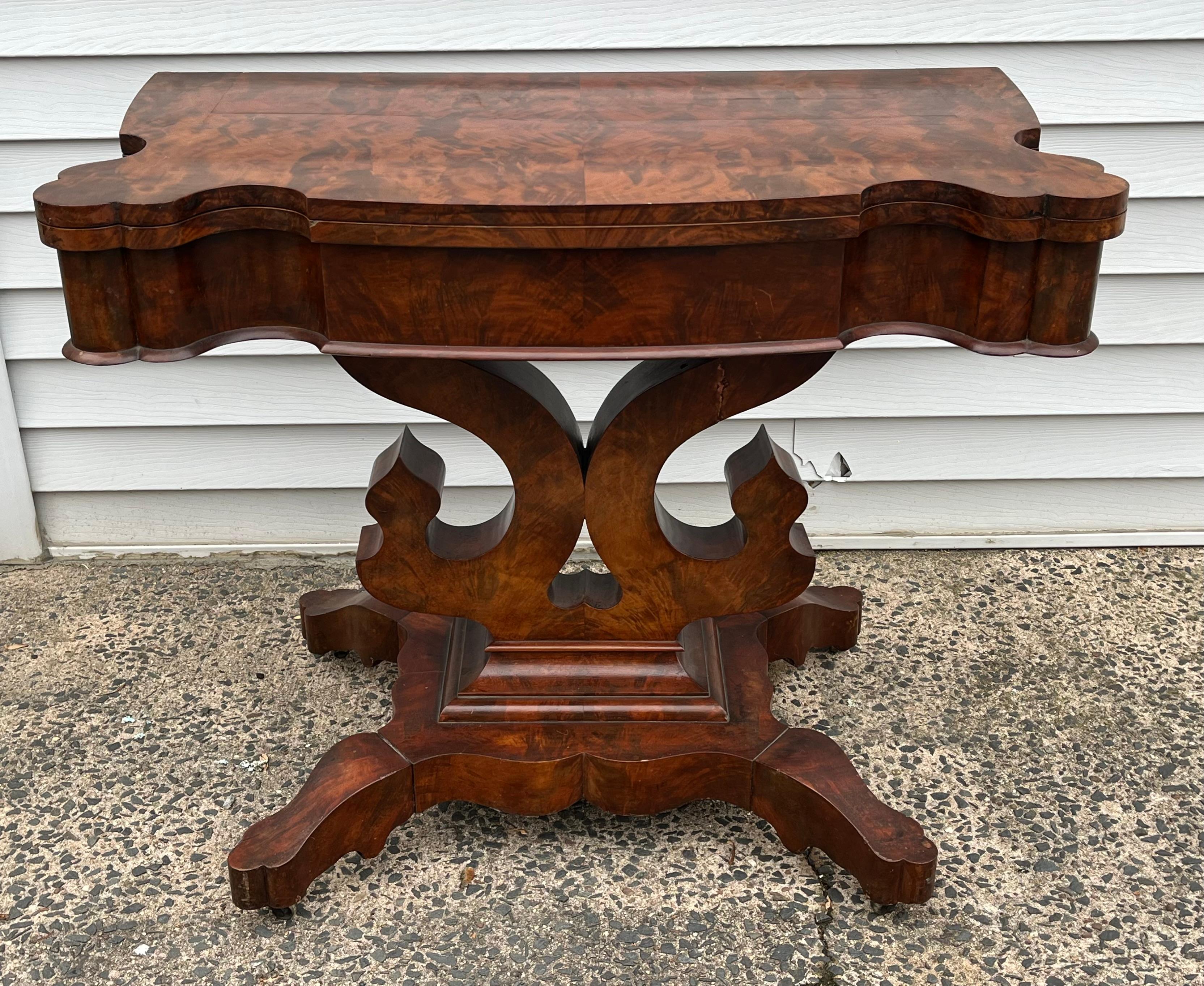 An American Empire flip-top console table in flame mahogany, circa 1870, with lyre base on plinth base with casters, converts to a 36” x 38” tea table. 