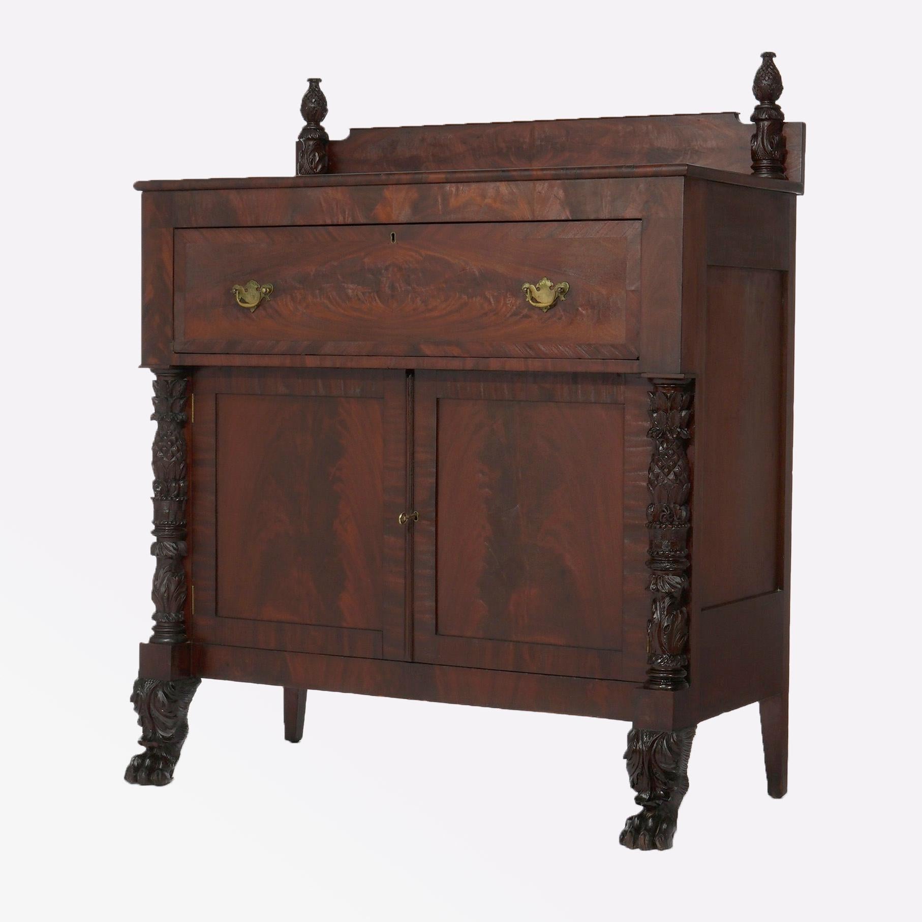 An antique American Empire Greco linen press sideboard offers deeply striated flame mahogany construction with backsplash having flanking finials over case with deep upper drawer surmounting double door lower cabinet and having flanking columns with
