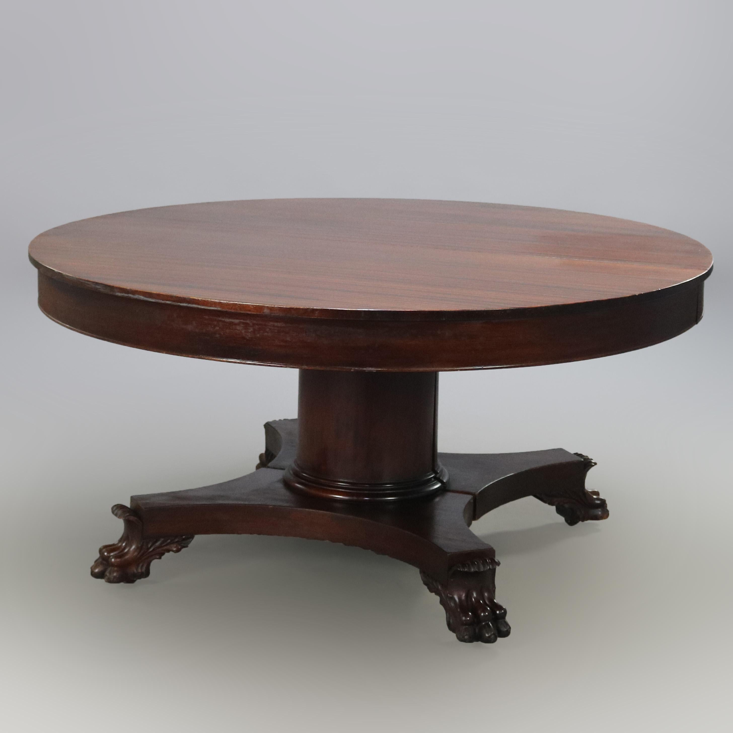 An antique oversized American Empire extension banquet dining table offers mahogany construction with split pedestal raised on carved paw feet, includes eight 12
