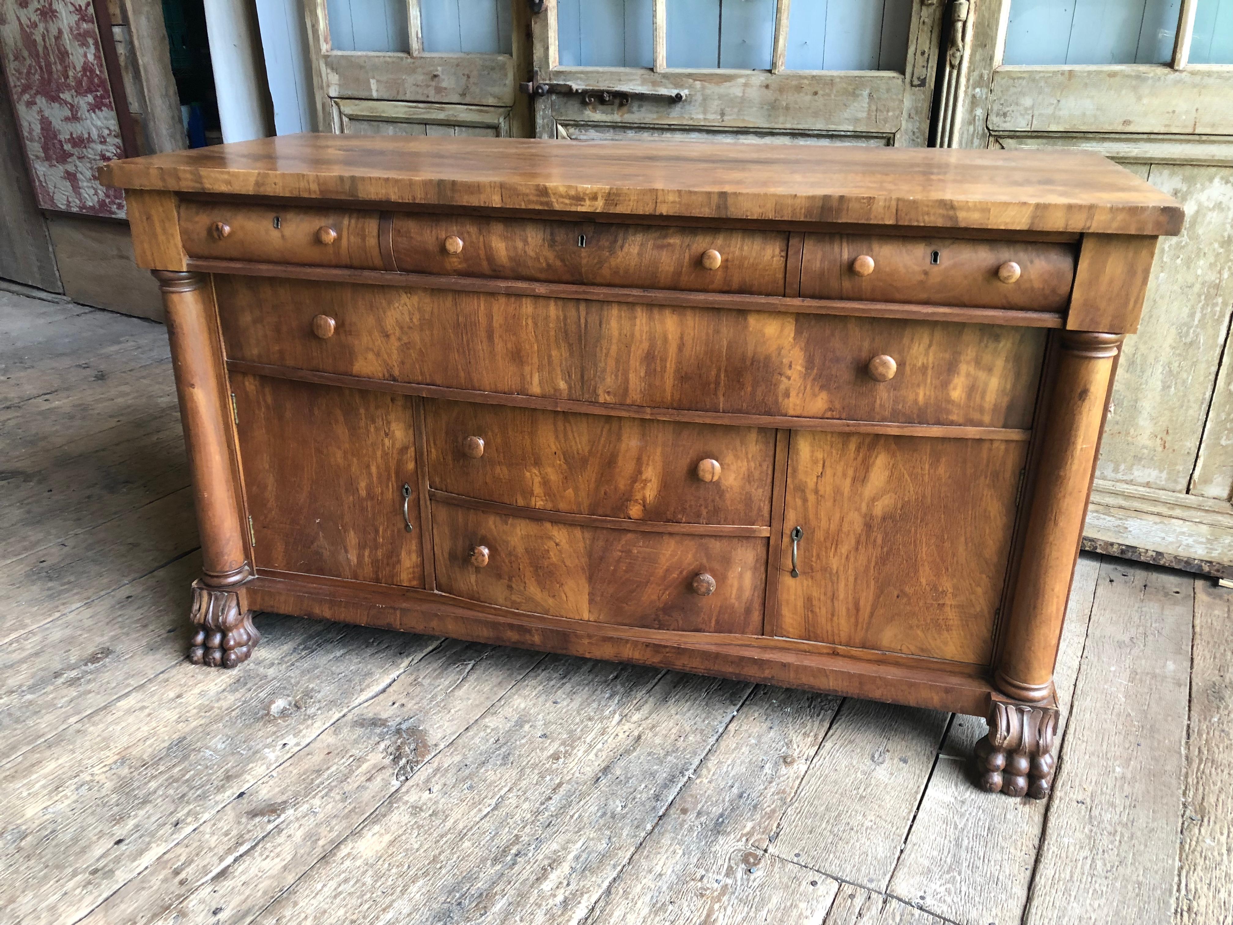 A nice American Empire sideboard in light walnut veneer, with 5 short drawers, one full length drawer and two cabinets, with column form supports and carved lion’s paw feet, circa 1870.