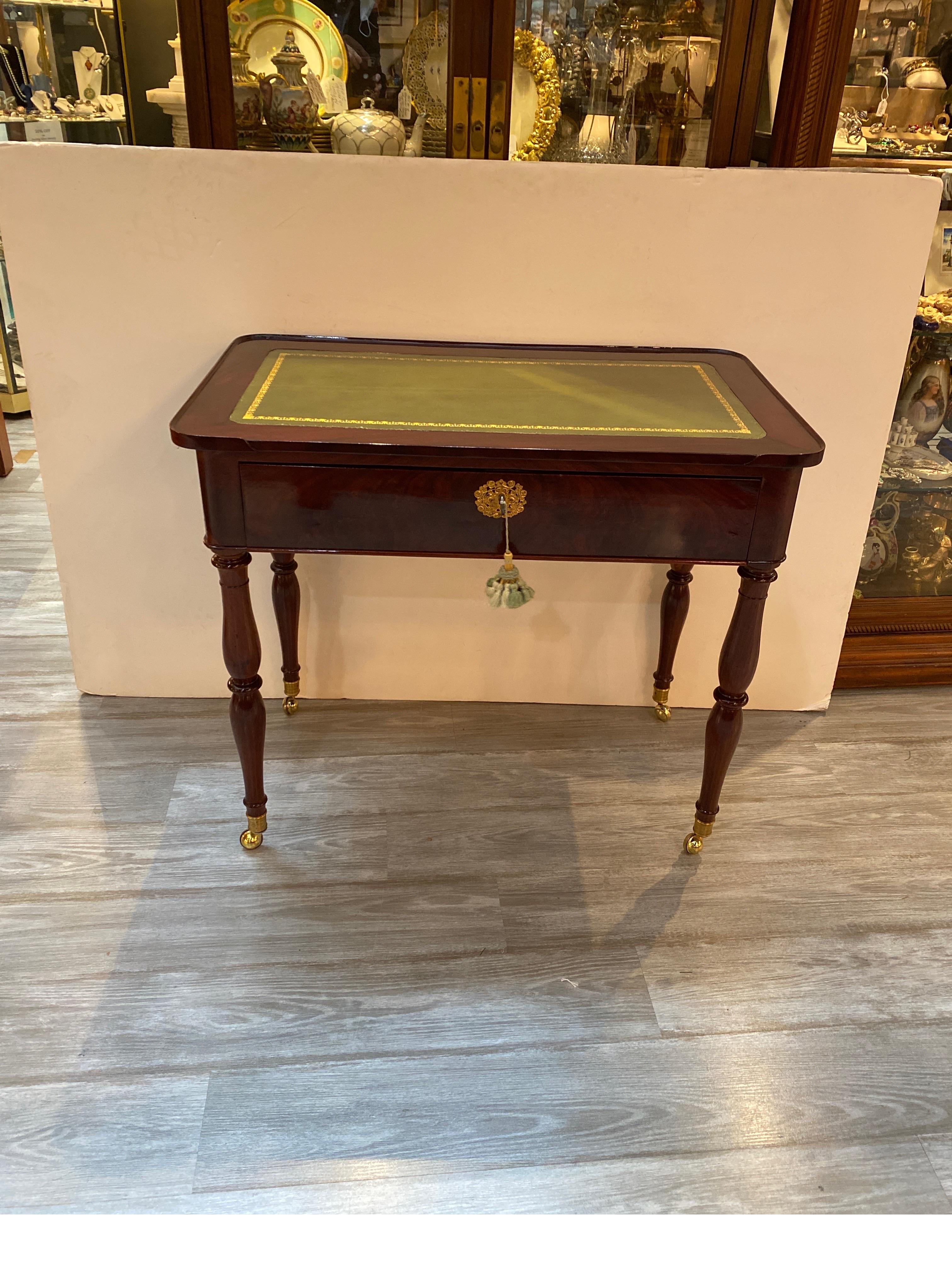 An elegant mahogany diminutive console deask with olive leather top. The retangular top with gilt tooled edge with central drawer with key, resting on four sold wood turned legs. 32.25 inches wide, 19 inches deep, 29.5 inches tall.