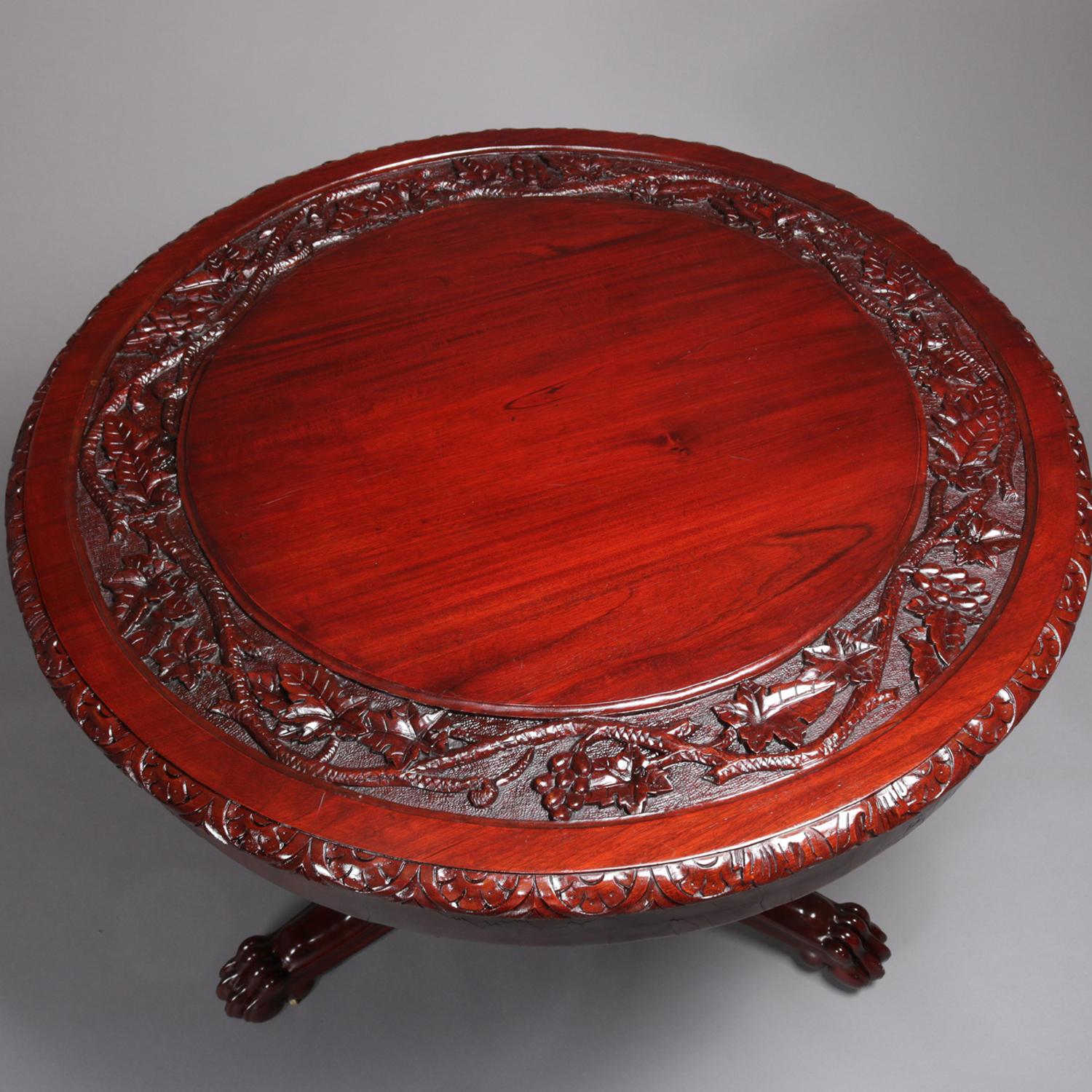 American Empire style classical carved mahogany center table features top with deeply carved grape and leaf wide interior bordering and foliate carved edge over broad skirt, raised on urn form pedestal and supported by three scroll form legs with