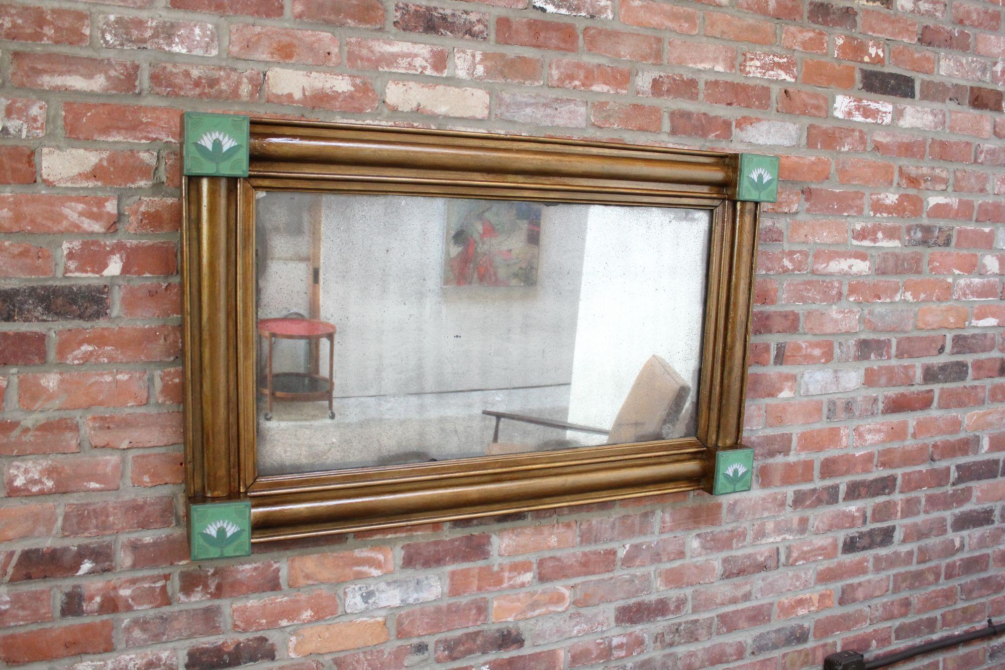 American Empire-Style giltwood mirror adorned in each corner with ceramic tiles depicting lotus flowers (ca. early 1930s, USA).
Glass is in distressed condition with foxing present throughout. Wear to the original gilt, as shown.
Remains an
