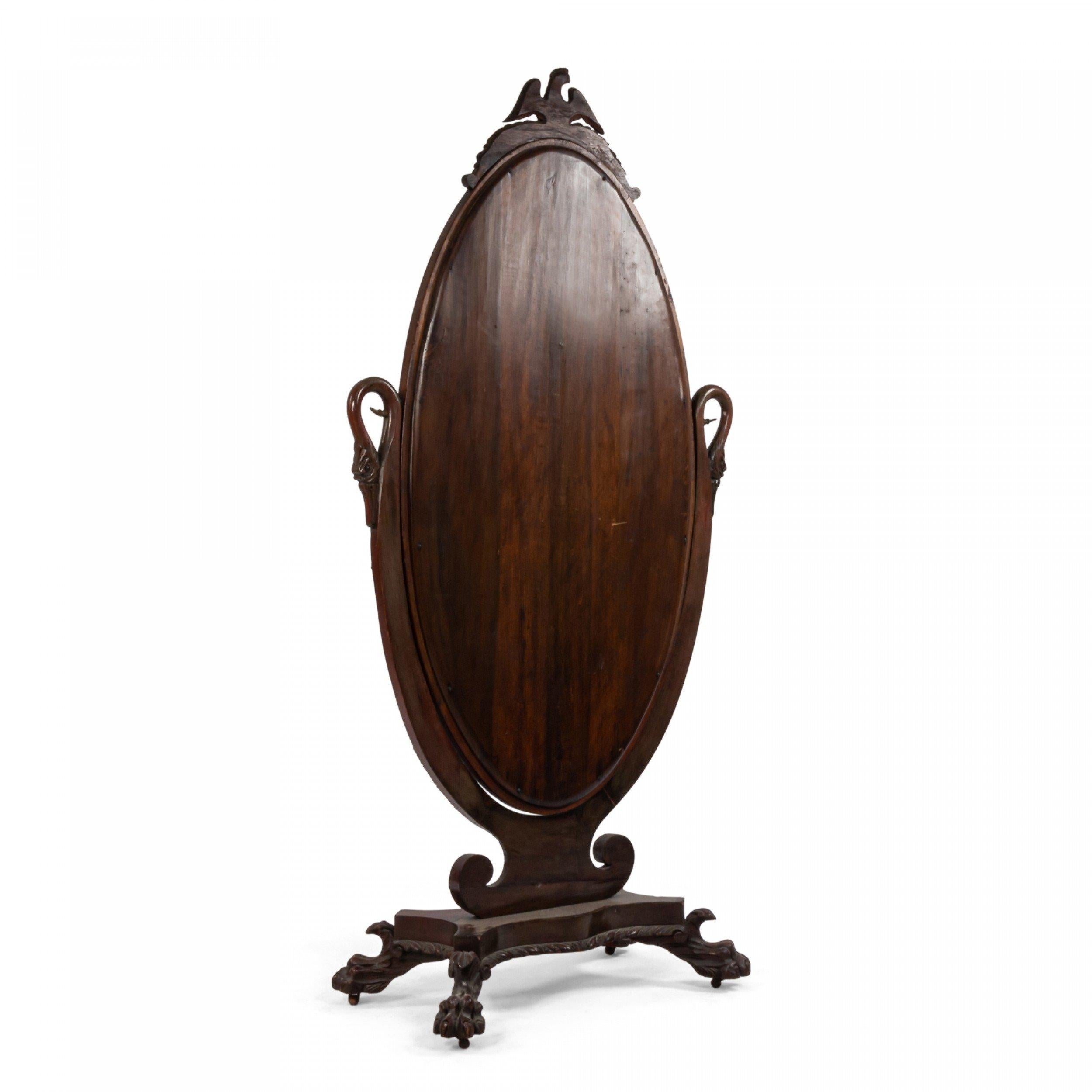 American Empire-style (first quarter 20th Century) mahogany cheval mirror flanked by carved swans on a scalloped base with paw feet and an eagle finial.