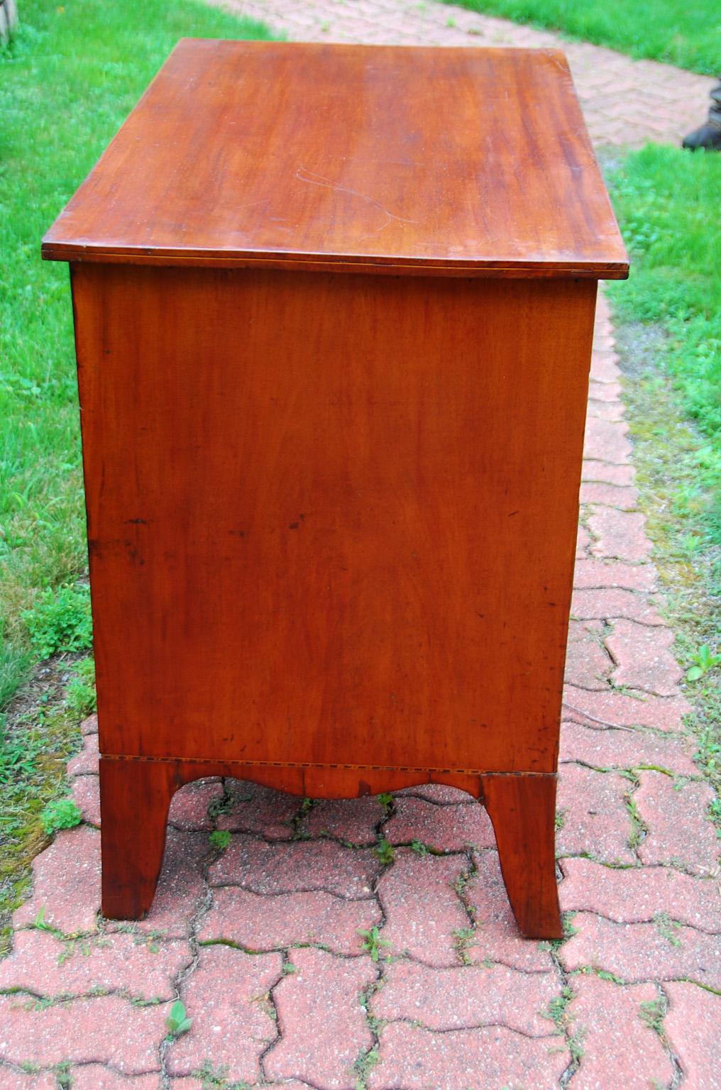 American Federal 18th century solid cherry chest of four graduated drawers with handsome shaped apron and splay feet. There is a checkered band of inlay to the base; a narrow line of boxwood stringing to the top edges, original oval brass and