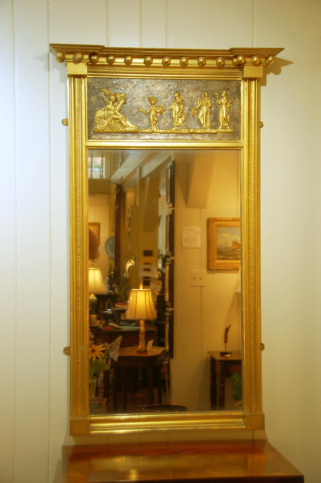 American Federal 18th century gold leaf mirror with bold cornice from which are suspended gold leafed balls. The cornice helps to frame a handsome bas relief panel with classical scene of Athena in her chariot and four approaching figures on a dark