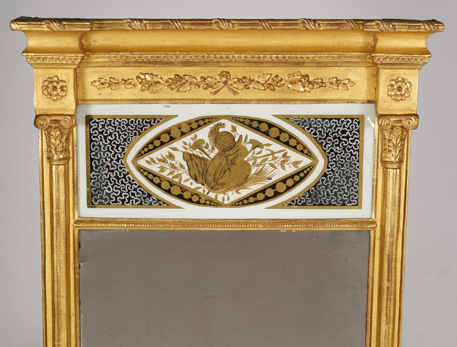 This Federal period giltwood pier mirror, dating to circa 1820, is designed in the architectural style. It features an elegant projecting crest molding with applied classical ornaments and rosettes above an églomisé panel with a classical motif.