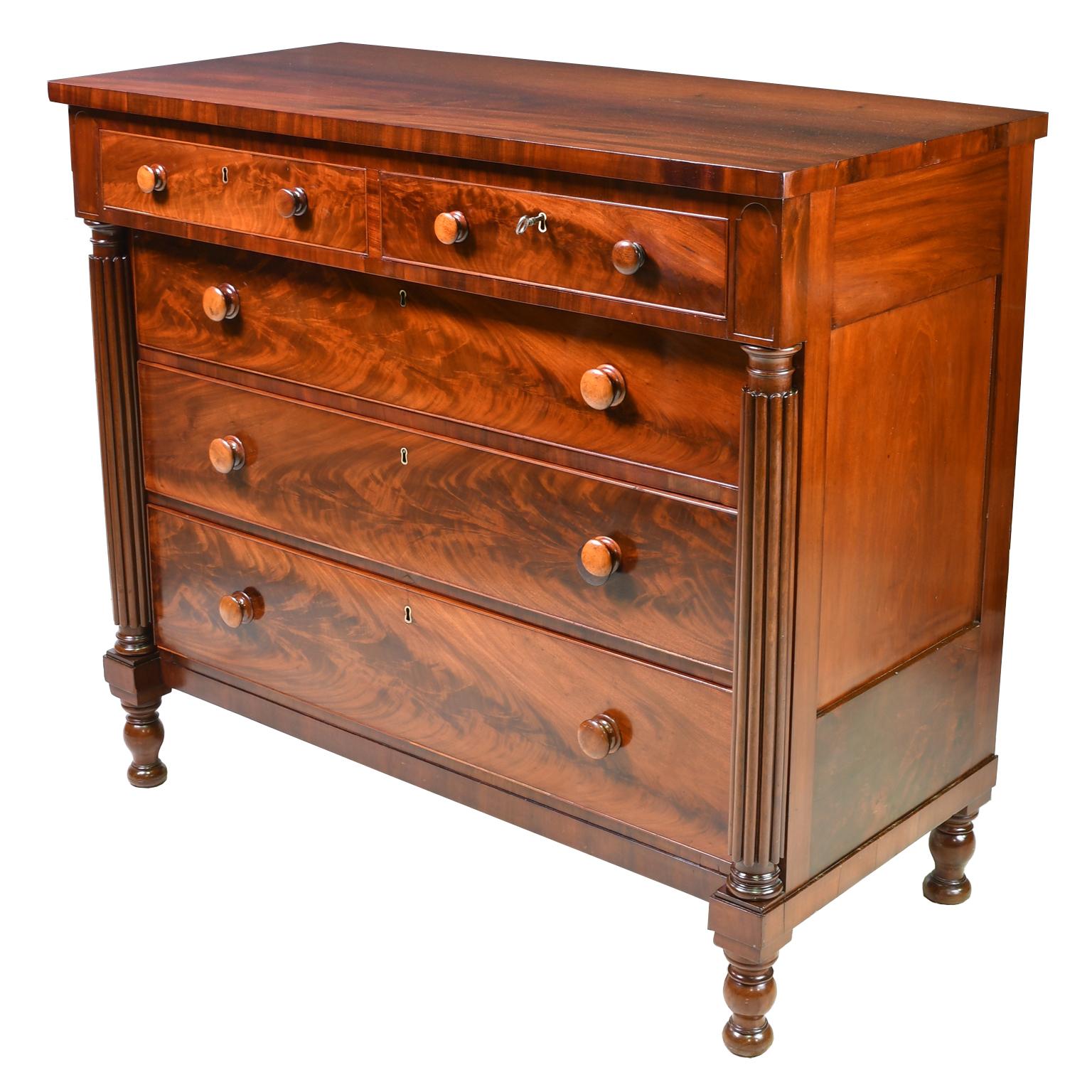 From the Federal period, a very beautiful American Neoclassical chest of drawers in fine West Indies mahogany with two overhanging small drawers supported by turned and reeded columns above three large drawers, all with round wooden pulls. The sides