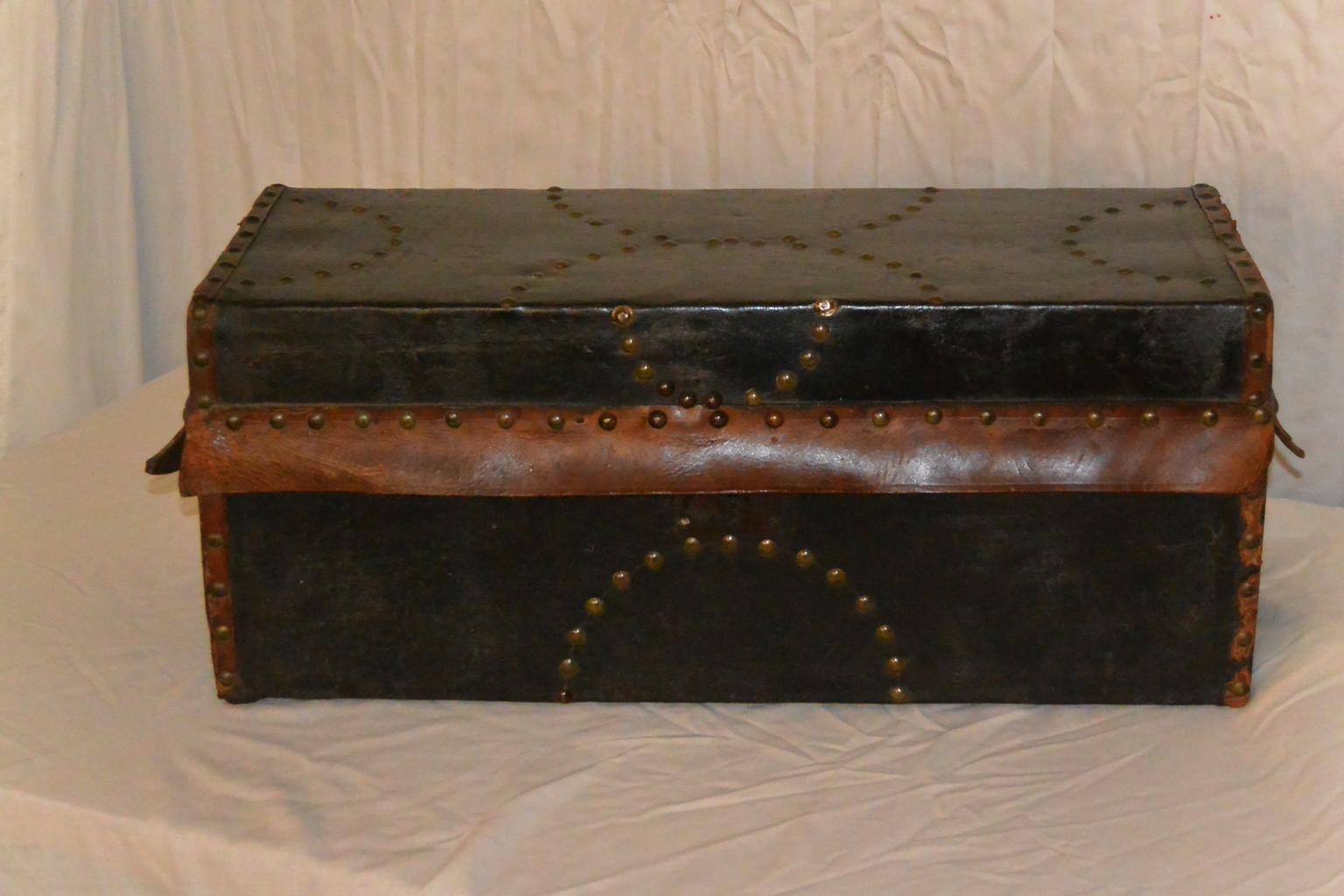 American federal child's trunk, black leather covering with natural colored leather bindings and brass tack decoration.  This early trunk has remnants of its original  blue colored paper liner with leaves, flowers and  oddities painted or printed on