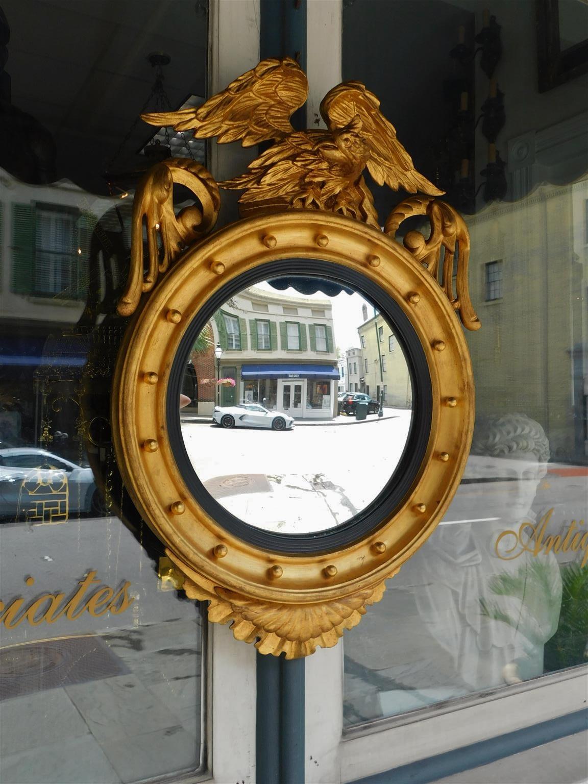American Federal gilt carved wood and gesso convex mirror with perched eagle to flee, flanking acanthus scrolled foliage, interior circular spheres, ebonized reeded ring, and terminating with a decorative intertwined floral pendant. Mirror retains