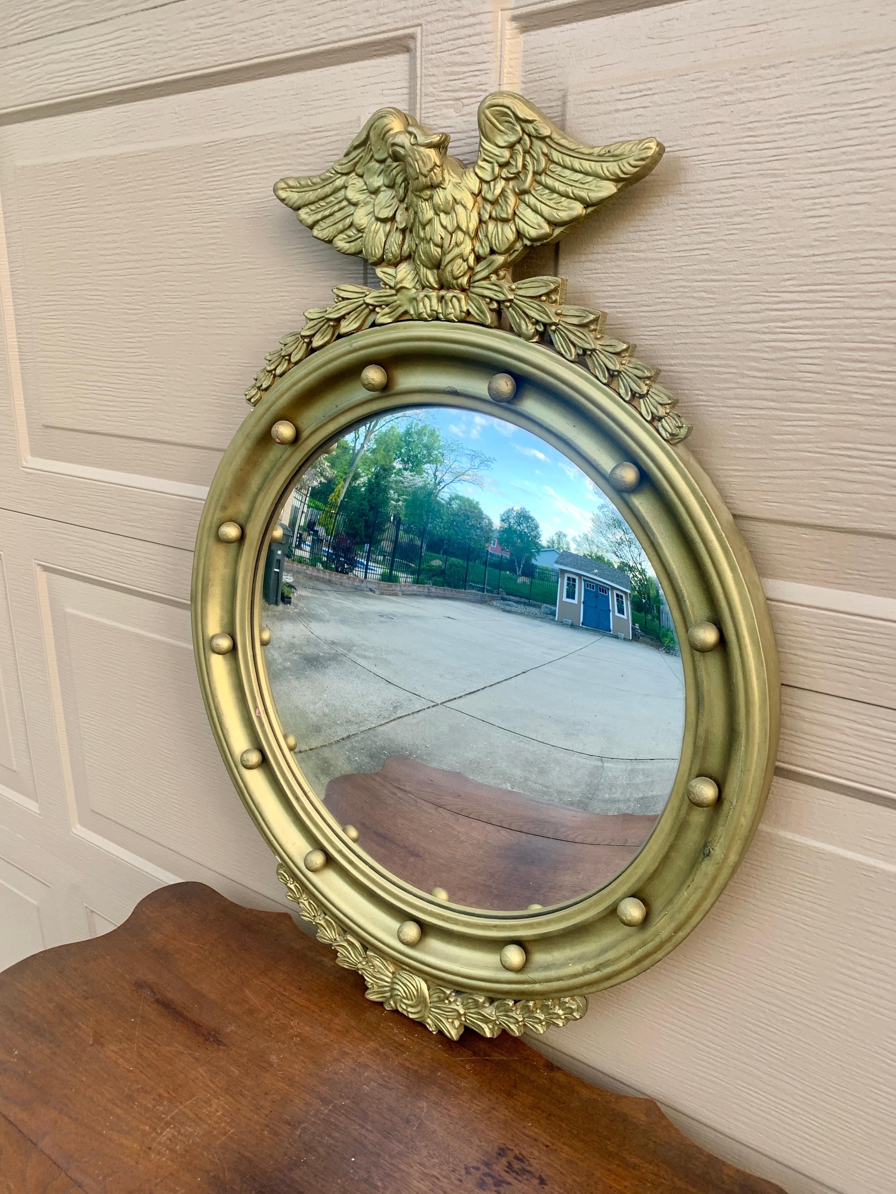 A gorgeous Federal or Regency style convex bullseye wall mirror featuring a carved eagle with open wings standing on olive branches and 13 small spheres representing the original 13 colonies around the inside perimeter.

USA, Mid-20th