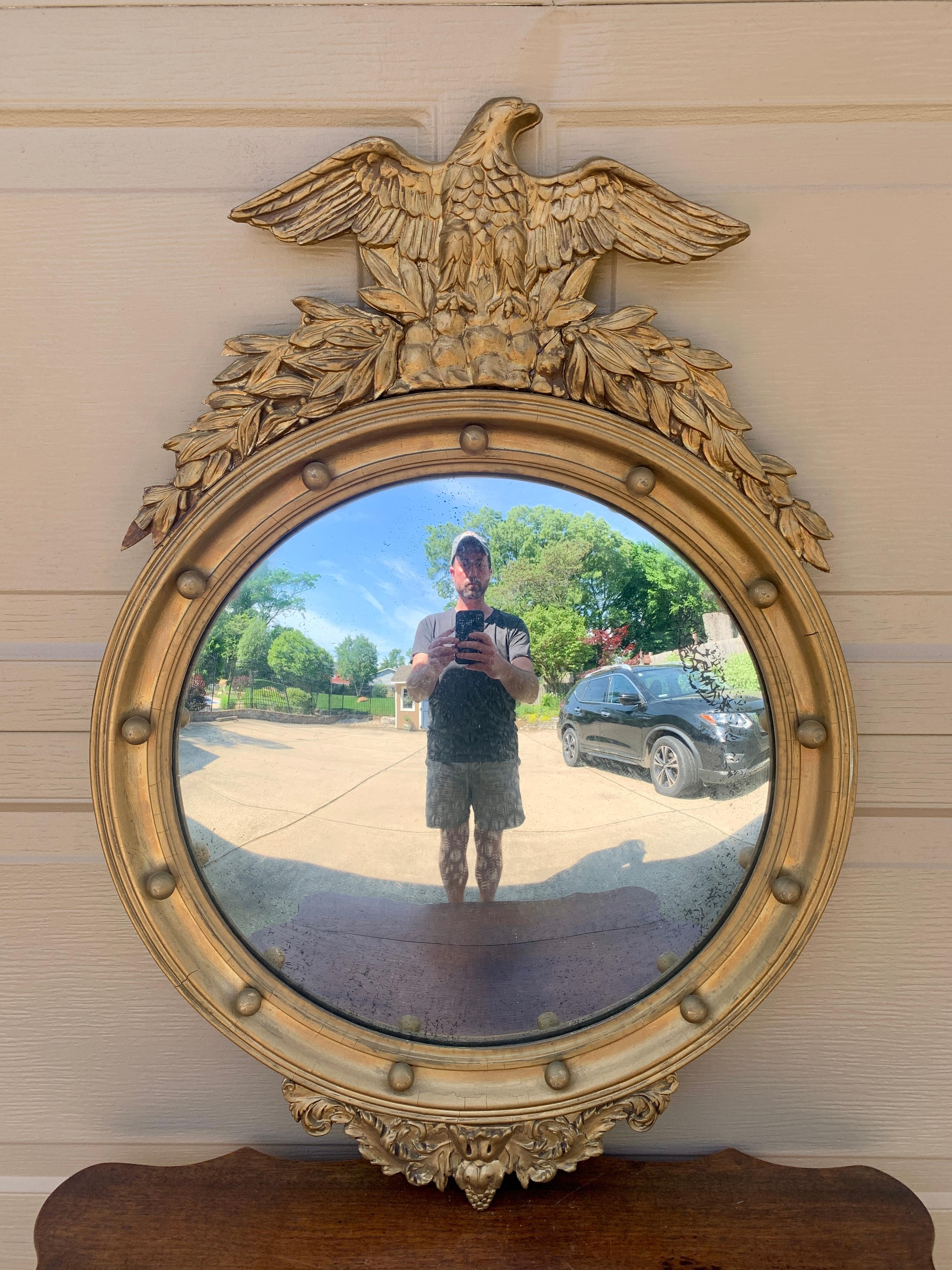 A gorgeous Federal or Regency style convex bullseye wall mirror featuring a carved eagle with open wings standing on olive branches and 13 small spheres representing the original 13 colonies around the inside perimeter.

USA, Mid-20th