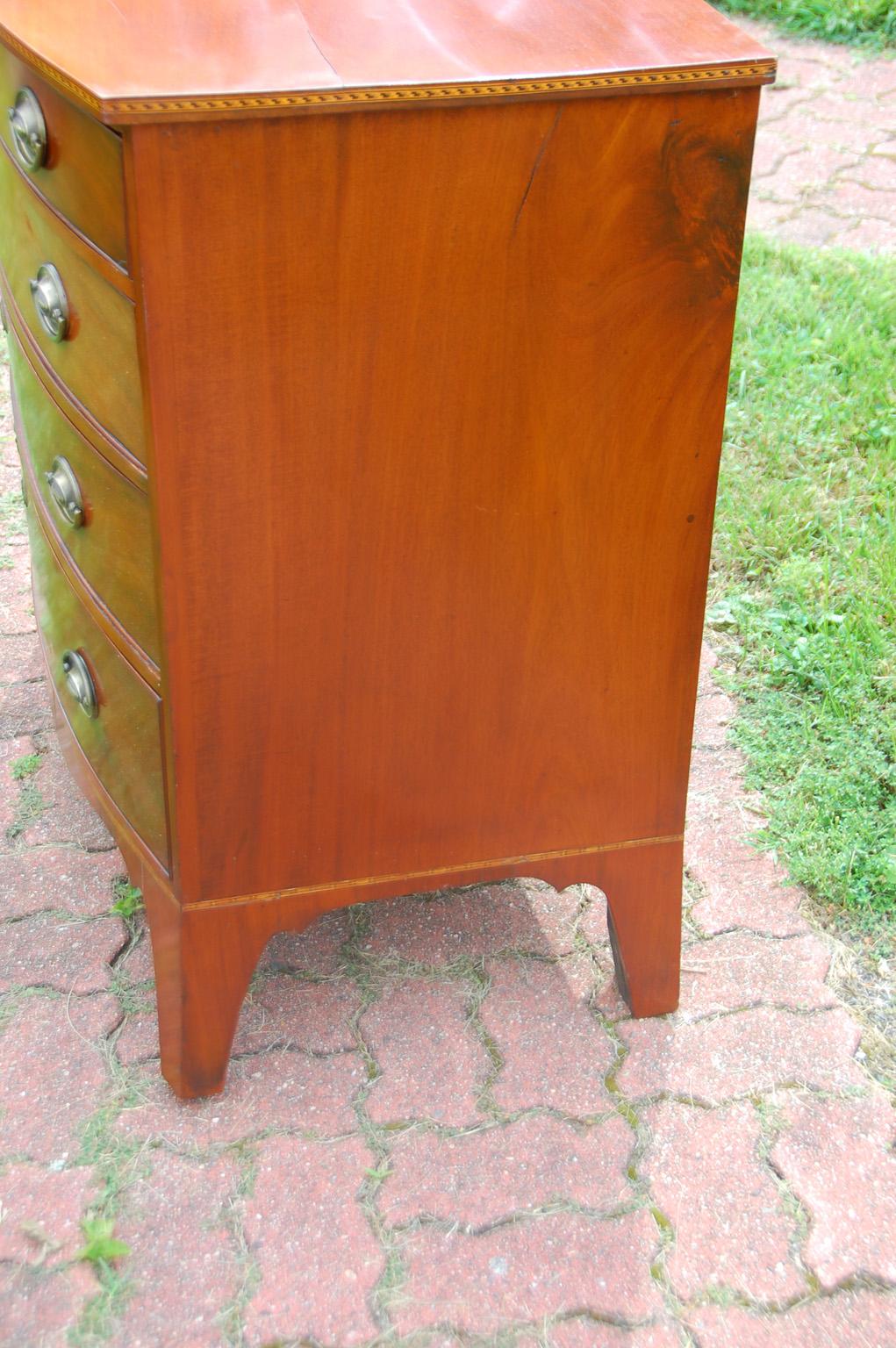 American Federal Hepplewhite period mahogany bowfront chest of four graduated drawers. This American chest has intricate narrow inlaid banding in lighter woods to the top edge of the top of the chest, as well as to the skirting of the chest. The