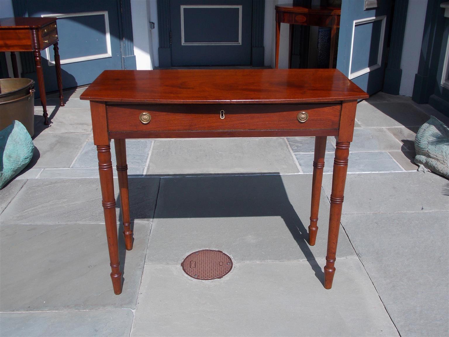American Federal mahogany bow front one-drawer server with a one board top, original brass floral pulls and escutcheon, and resting on the original turned bulbous ringed legs, Early 19th century. Secondary wood consists of white pine, 