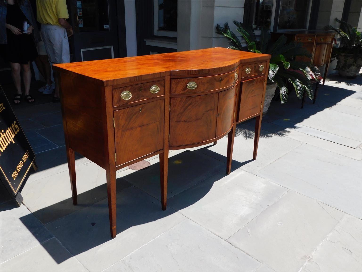 American Federal mahogany bow front sideboard with three frieze drawers over centered hinged cabinet doors, flanking hinged doors with fitted interior single drawers, period brasses, interior locks with keys, and terminating on tapered legs with