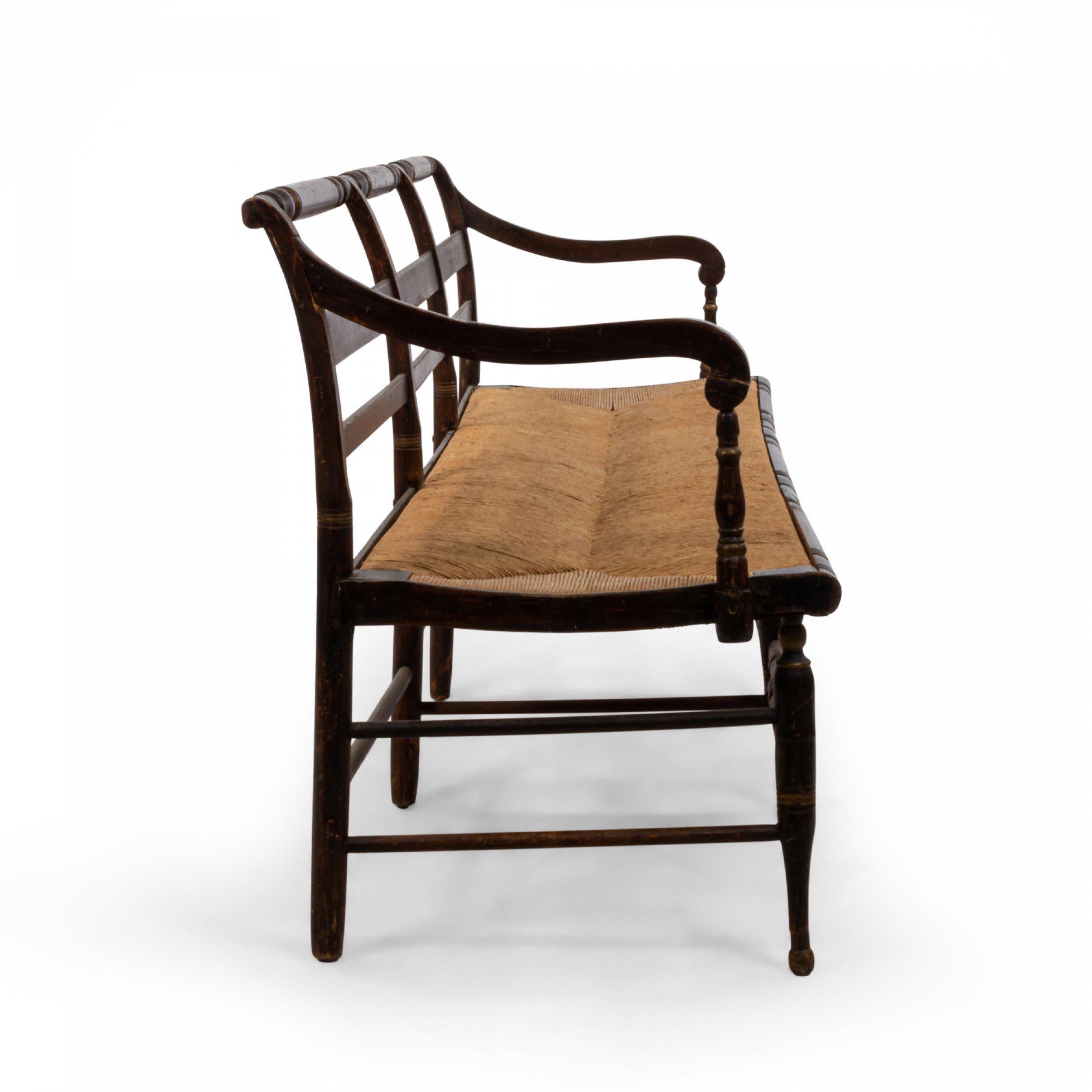 American Federal (First half of the 19th century) dark brown painted and gold stencil decorated bench with ladder back and rush seat supported on eight turned legs connected with a stretcher.