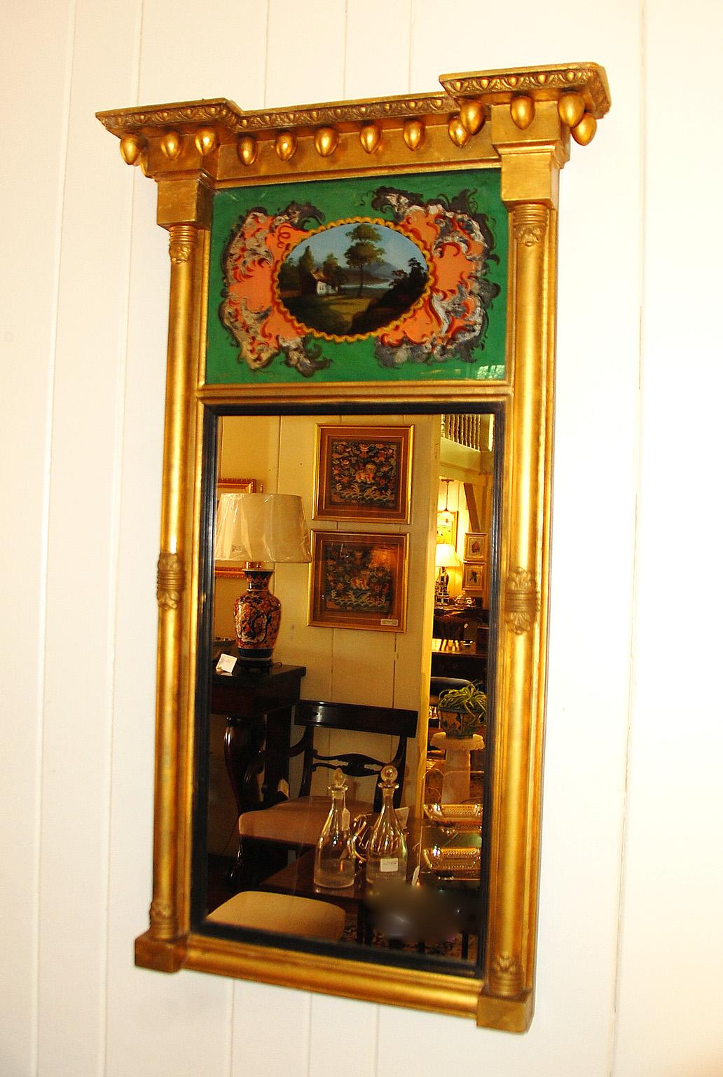 American federal period eglomise gold leaf mirror. The eglomise scene is of a cottage by a river with hills in the background in an oval, on a green ground, embellished with stylized silver acanthus leaves. There is some wear to some of the leaves,