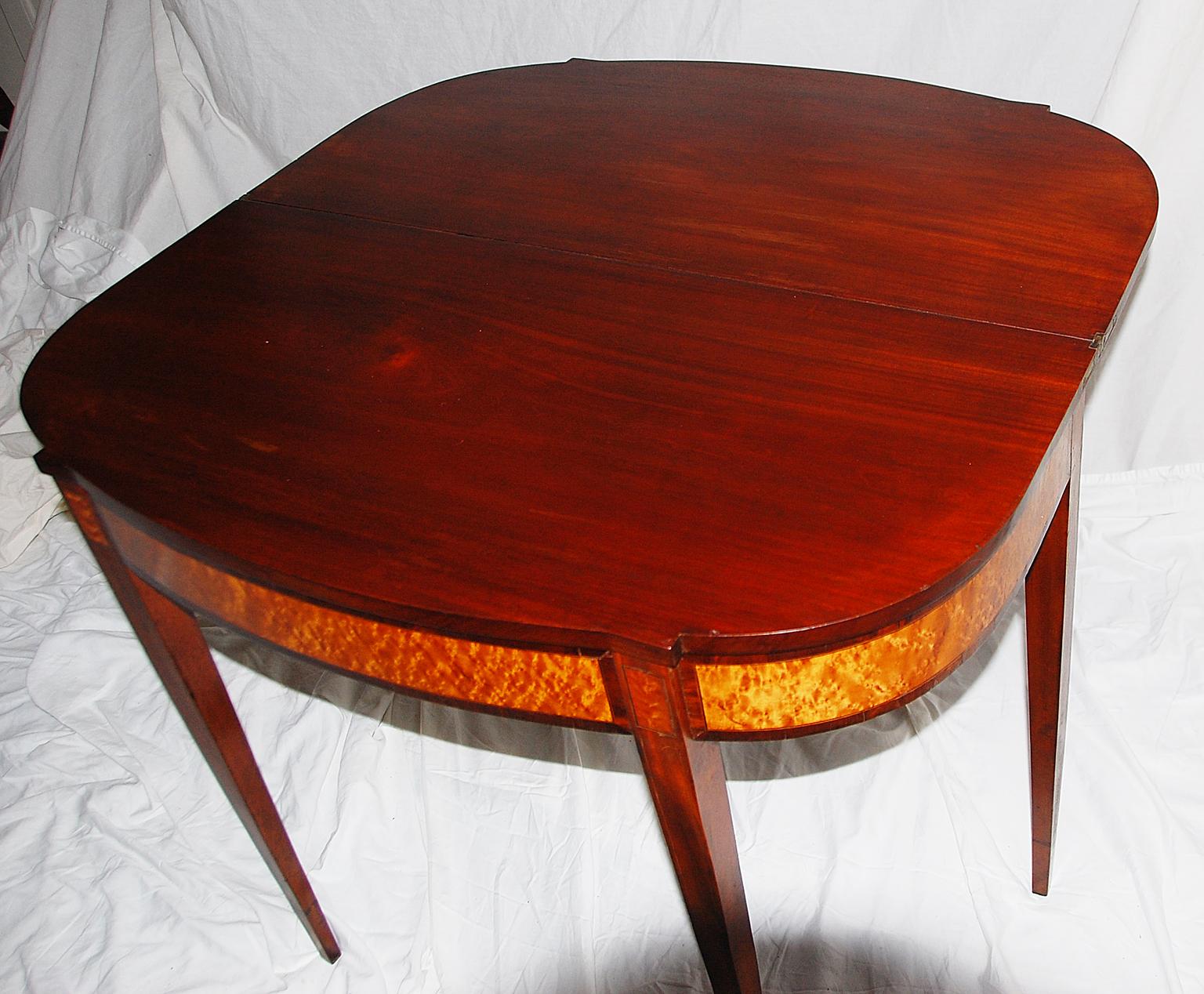 American Federal period Hepplewhite mahogany tea table of New England origin. The breakfront bowfront table is in mahogany with bird's-eye maple panels, ebony and boxwood stringing. One leg swings out to support the table when it is opened, it can