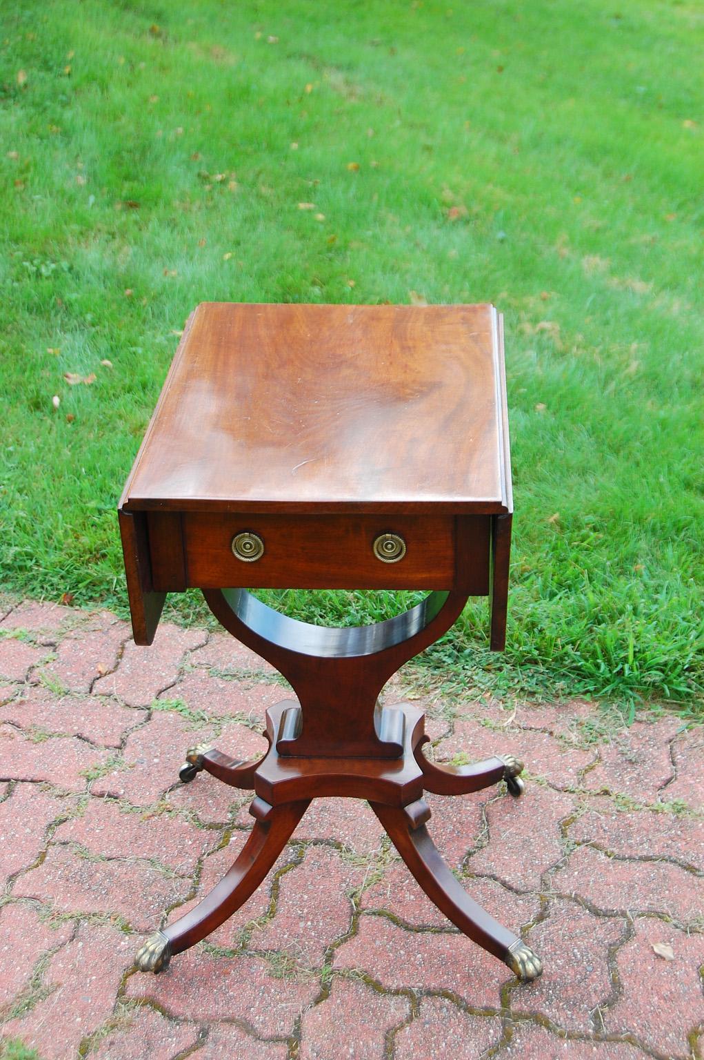 American federal period mahogany dropleaf sewing table with pedestal base supported by four graceful downswept legs ending in paw feet. A stylized curved cradle supports the upper case. This versatile sewing table has one drawer with the original