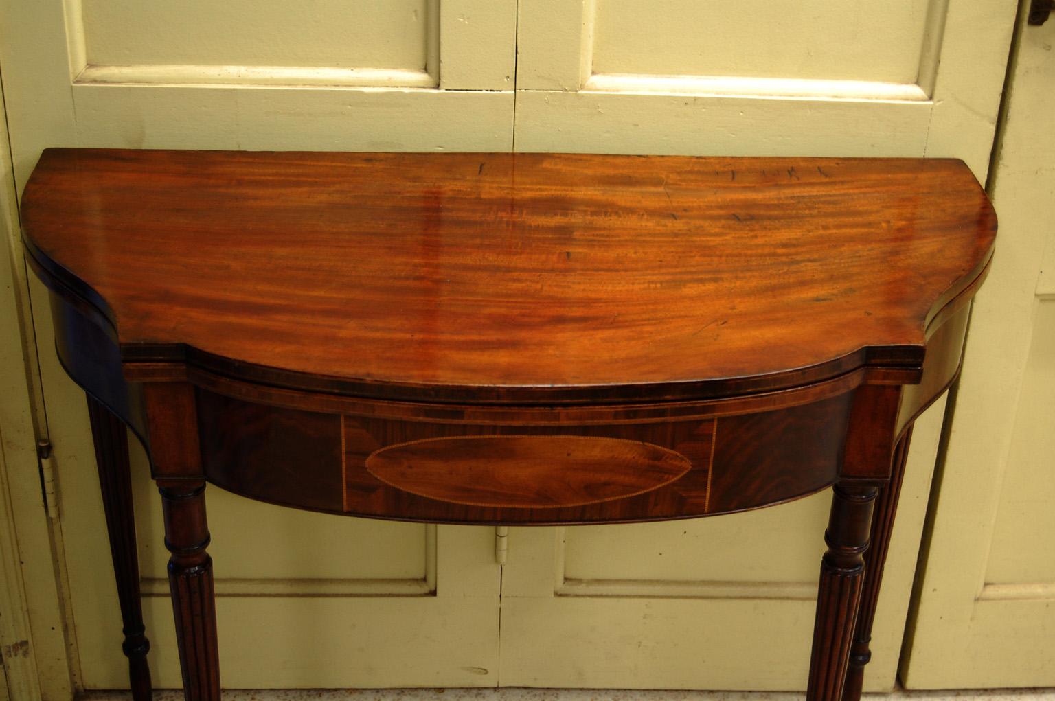  American Federal mahogany serpentine tea table with reeded legs, oval holly inlay with intricate stringing to skirt, stringing to the edge of the top.  The tapered reeded legs have a lower collar and below that instead of a straight taper for the
