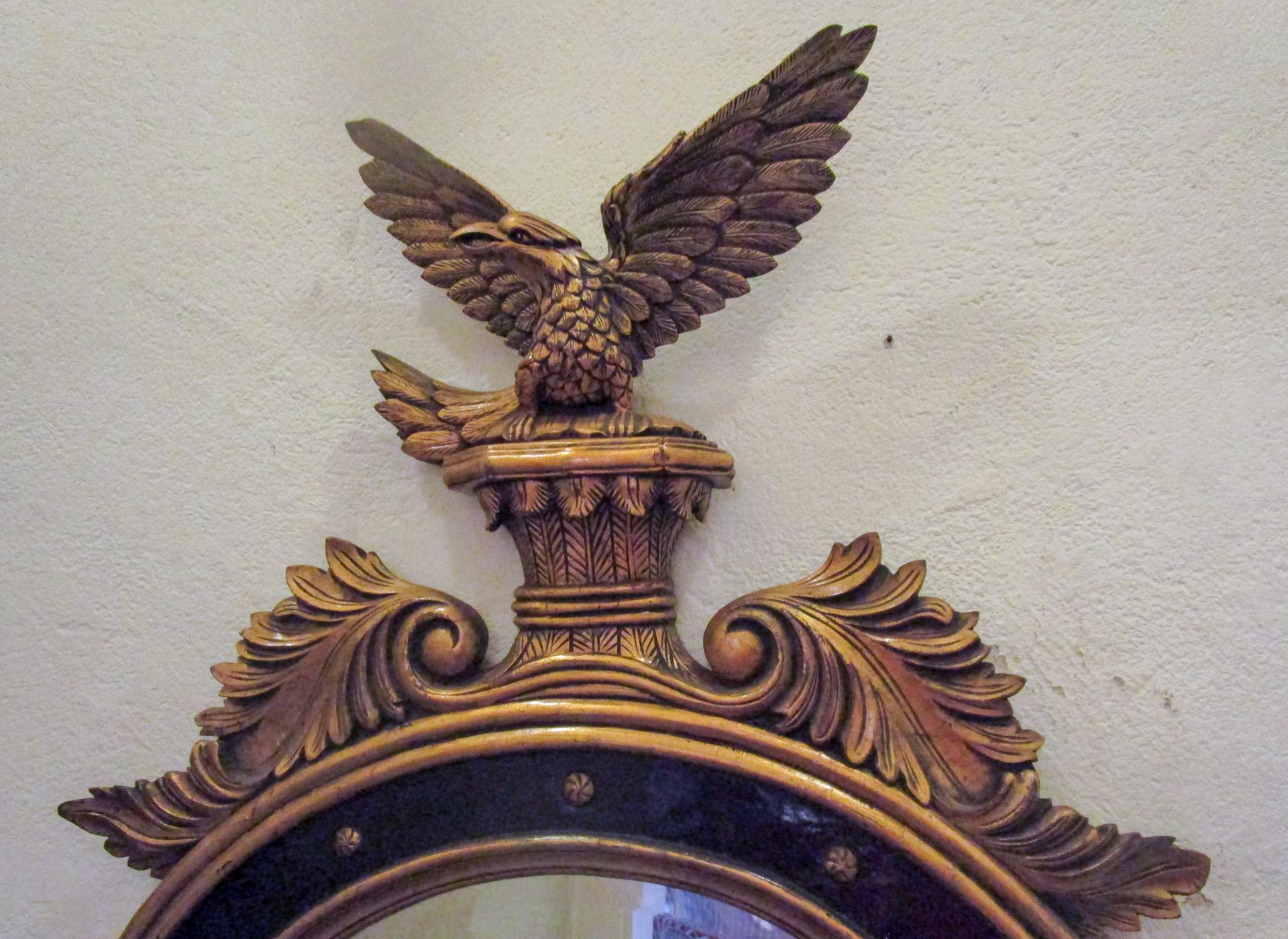 Ce miroir classique en bois doré américain de style Feder est finement sculpté et... 
représente un aigle aux ailes largement déployées, perché sur un piédestal. Des gerbes de blé et d'élégants rinceaux d'acanthe, tous deux symboles d'immortalité,