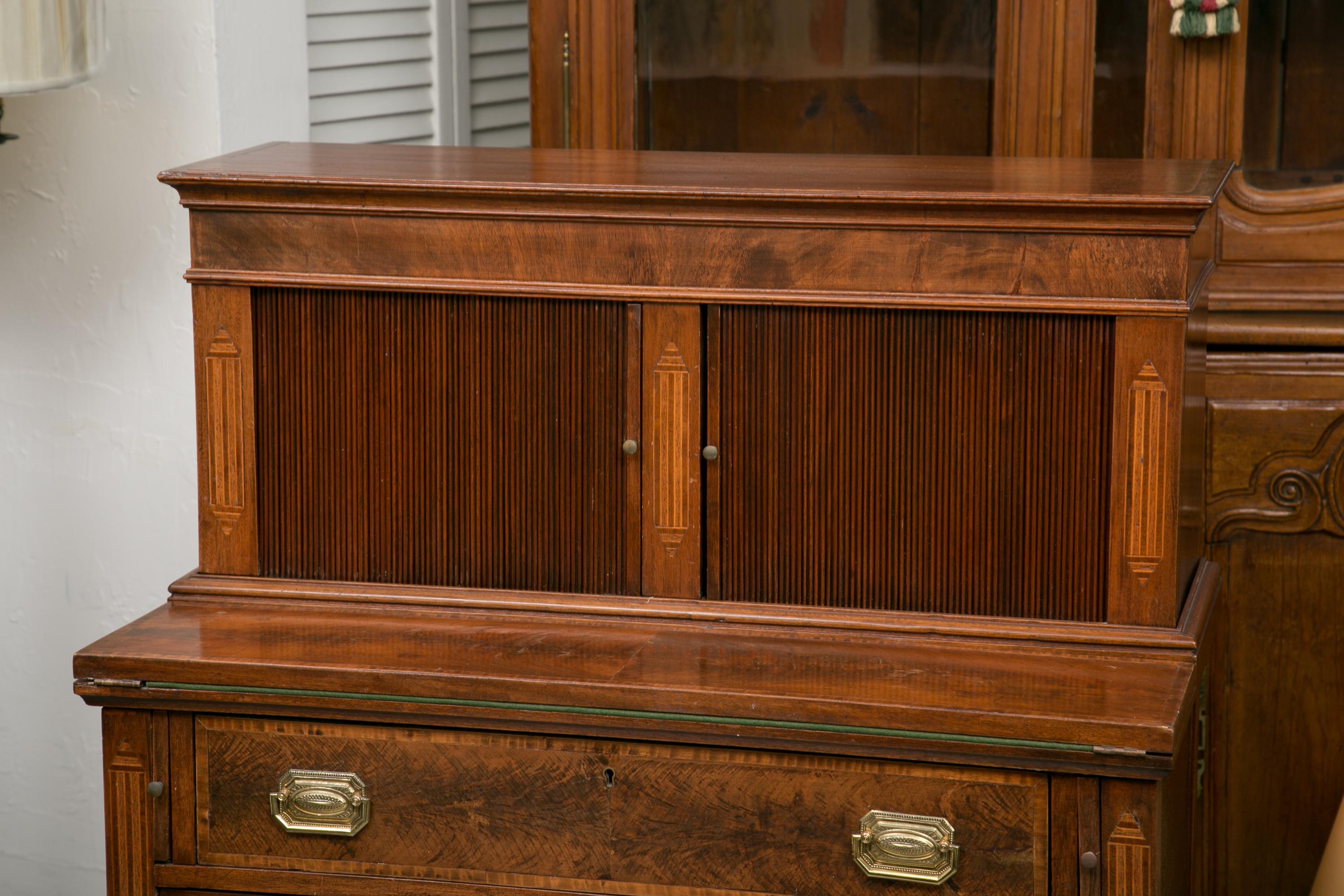 This is a Classic American Federal writing desk with a tambour door on the top section when open it reveals small drawers and document compartments. The bottom section has a fold over writing section with a felt surface and two long drawers below.