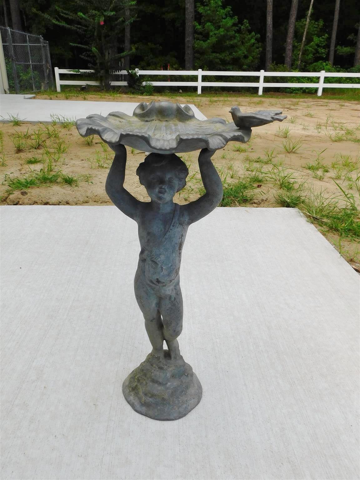 American figural boy lead bird bath holding shell above head with dove perched on rim while standing on a circular molded base, Mid 19th Century