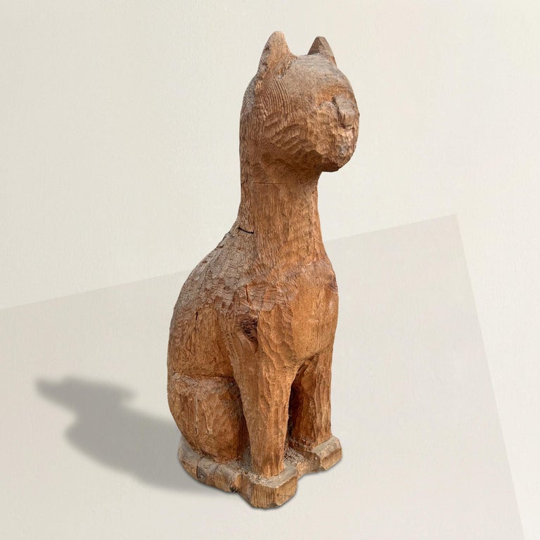A whimsical and bold 20th century American Folk Art cared wood sculpture depicting a stylized seated cat with a long neck, expressive face, and a beautiful chip carved surface. It crosses myriad stylistic genre including Art Deco, Modern, Folk Art,