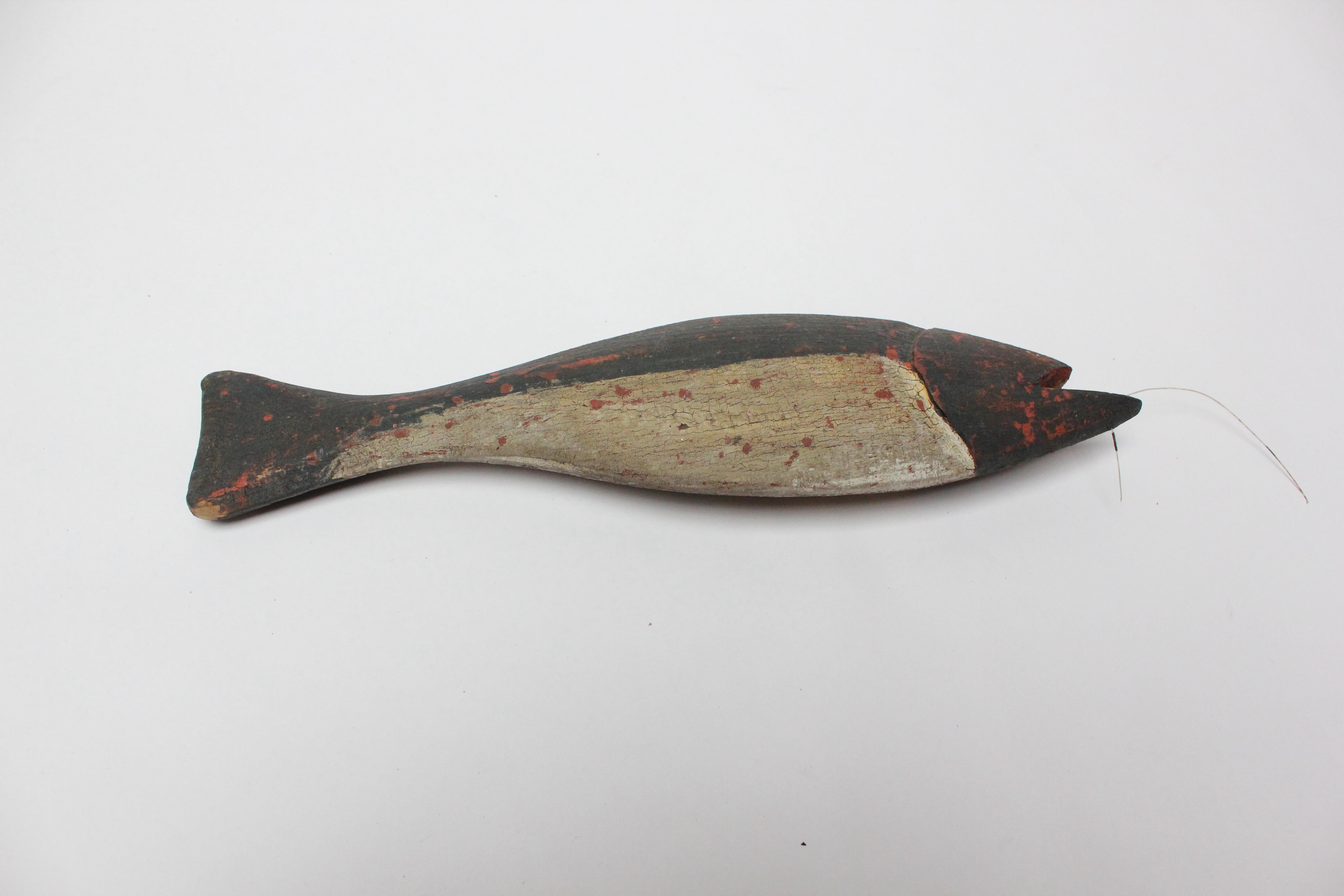 American Folk Art hand-carved and painted fish decoy with a fishing line in its mouth (ca. 1940s, USA). Natural patina, crazing, and paint loss present - the red base coat can be seen in spots where the white or black paint has peeled. Remains a