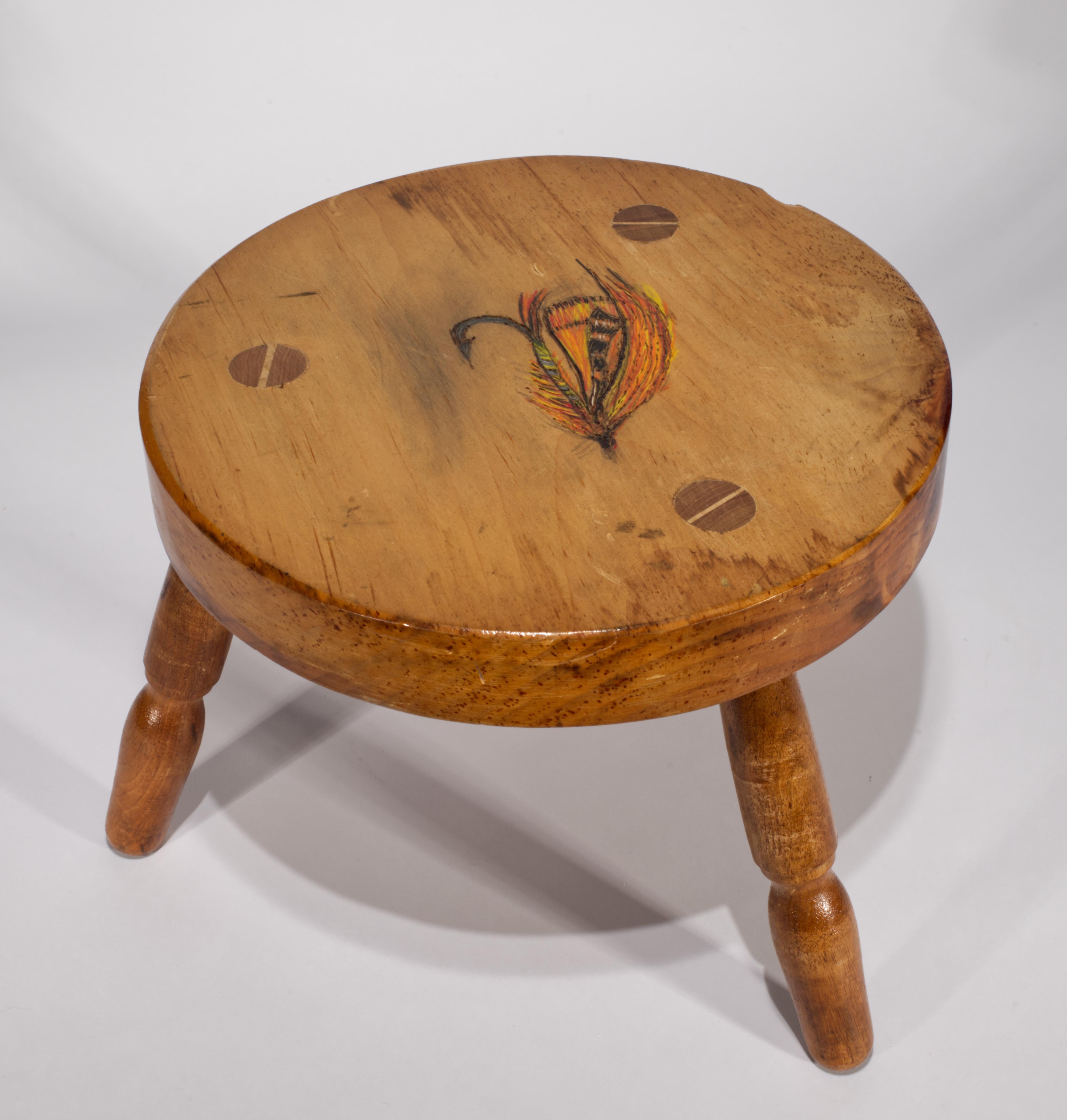 Lo sgabello rustico in legno è caratterizzato da un sedile rotondo in legno di pioppo massiccio su 3 gambe, che ricorda i tradizionali sgabelli da mungitura, e da un motivo dipinto a mano di una grande mosca da pesca al centro del sedile, circondato