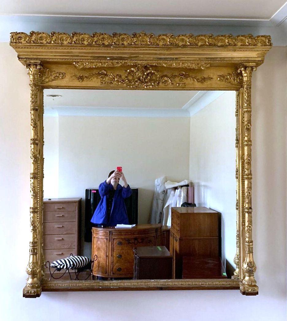 American Gilded Age period mantel mirror with heavy carved and giltwood frame. The heavily ornamented frame has floral elements and the pediment held up by columns has a multitude of acanthus scrolls. A Louis XVI style ornate ribbon is added to the
