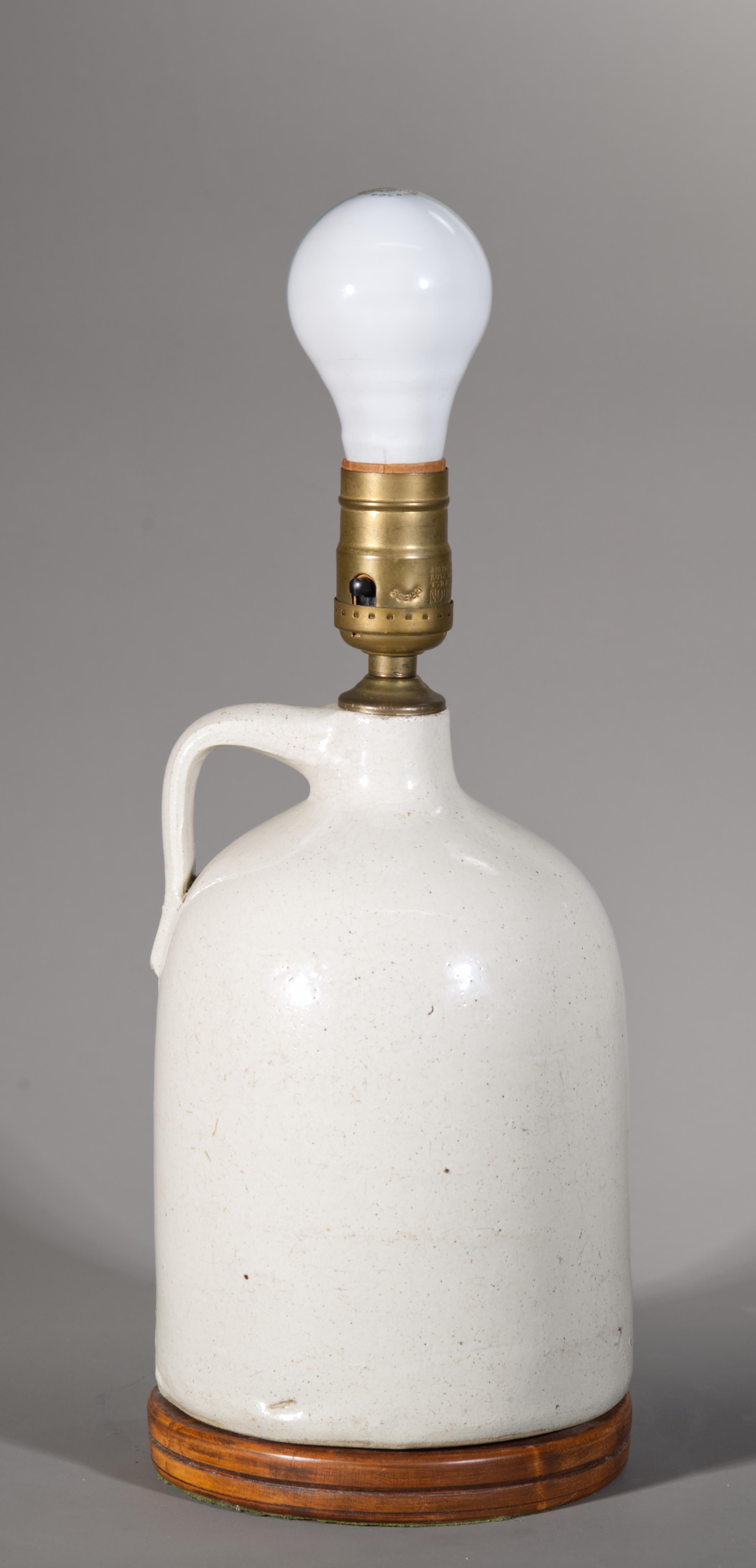 Antique or vintage glazed stoneware jug, converted into table lamp, features traditional shape with applied finger ring handle, rounded shoulders, and narrow neck; it is decorated in monochromatic off-white glaze with grey undertones. The lamp has